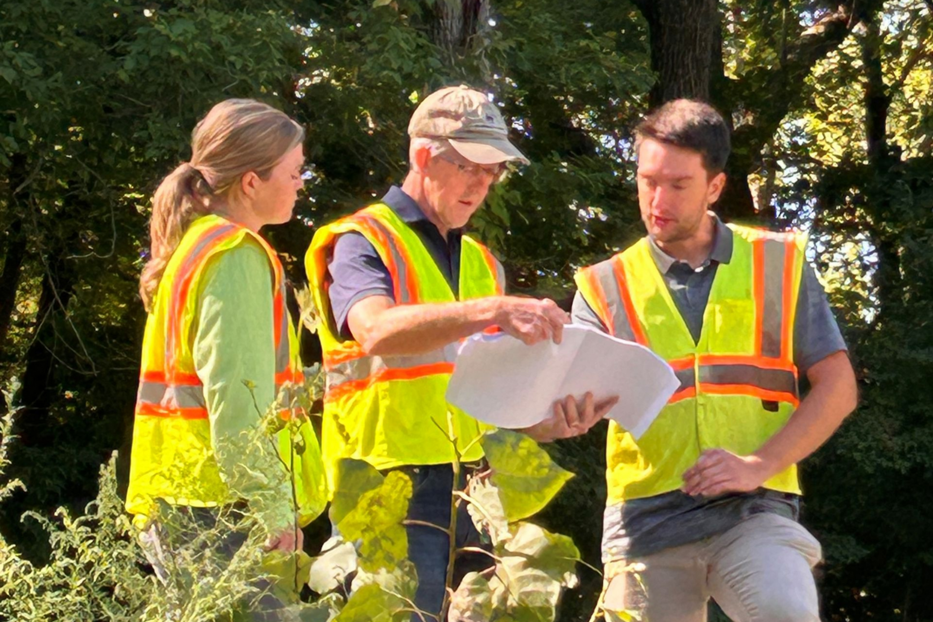 3 people in the field reviewing a plan together with high-vis safety vests on