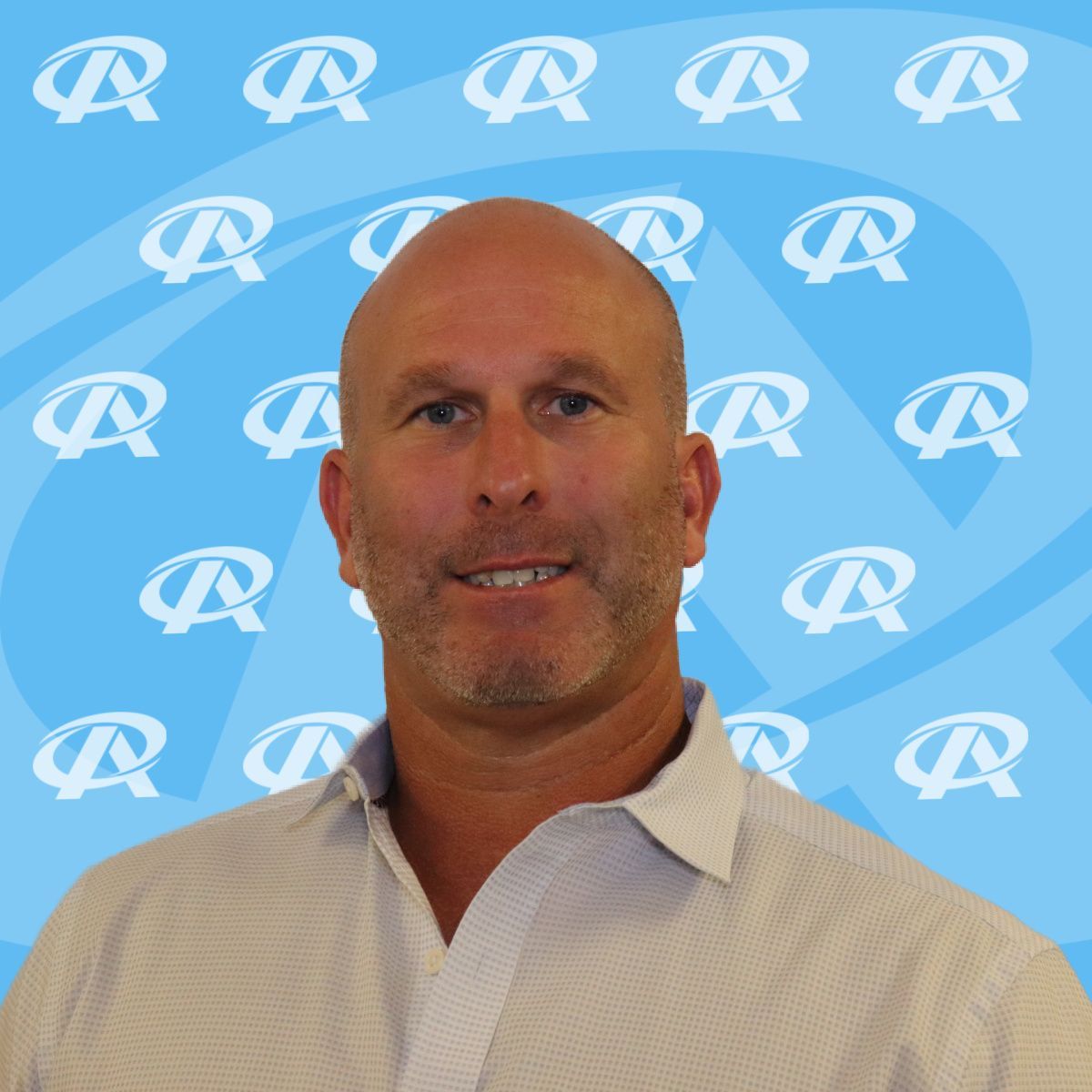 A bald man is smiling in front of a blue background with the letter r on it