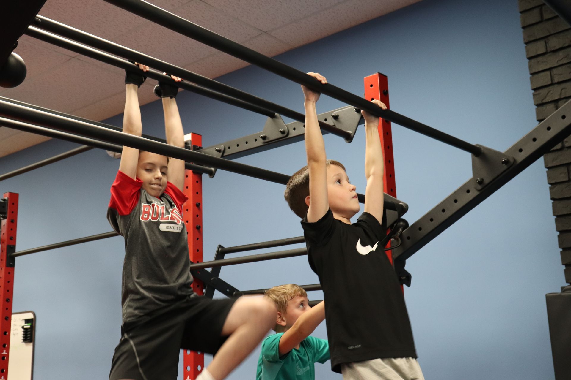 A boy in a nike shirt hangs upside down on a bar