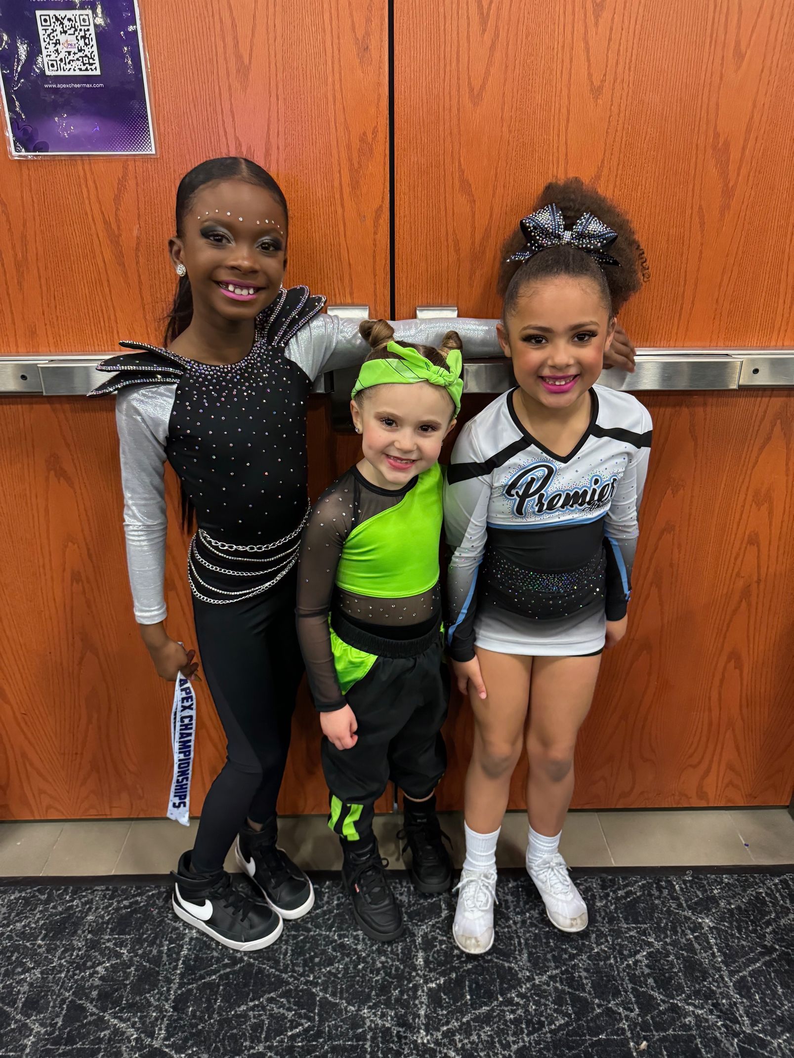 Three cheerleaders are posing for a picture in front of a wooden door.