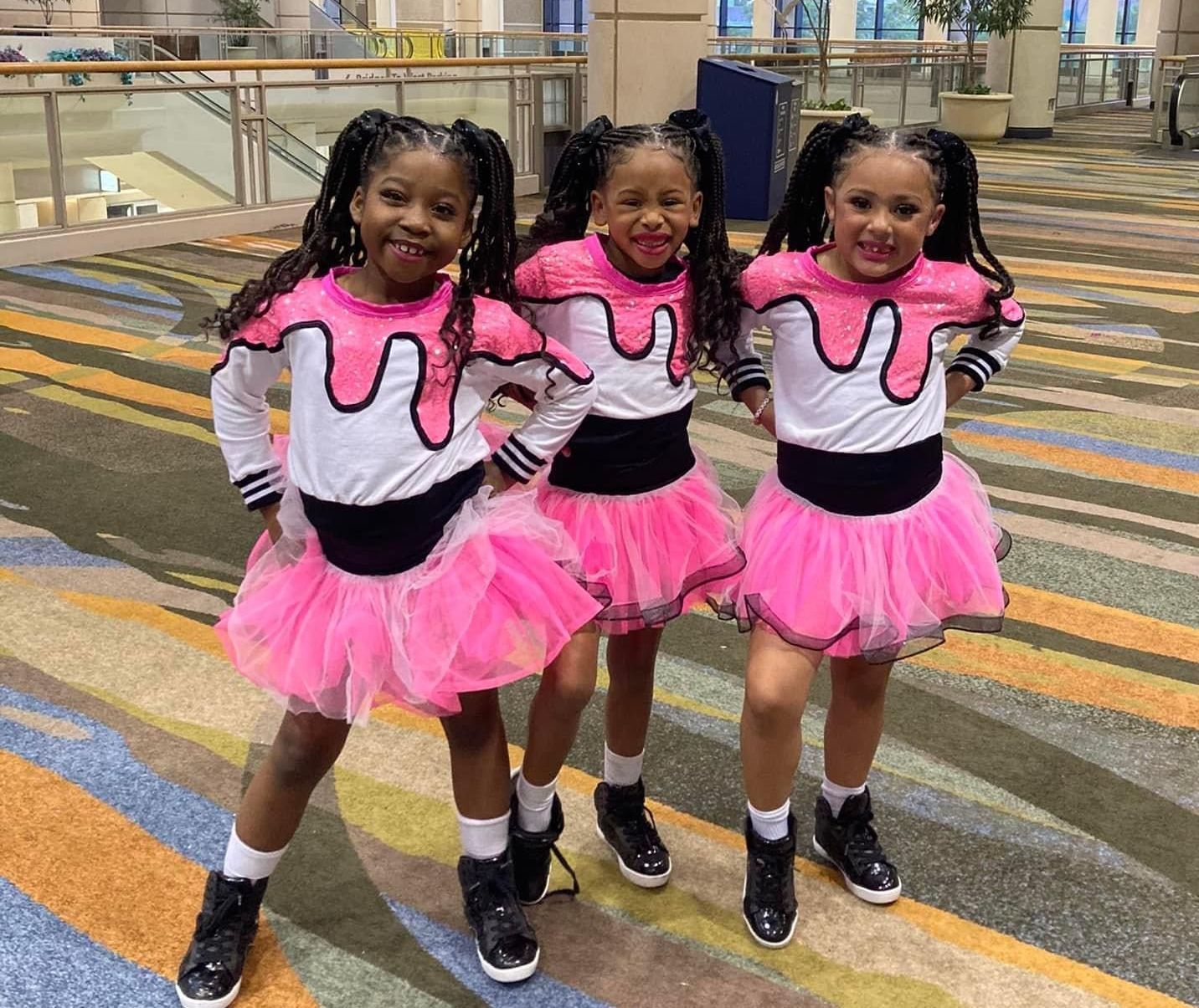 Three little girls are standing next to each other wearing pink tutus.