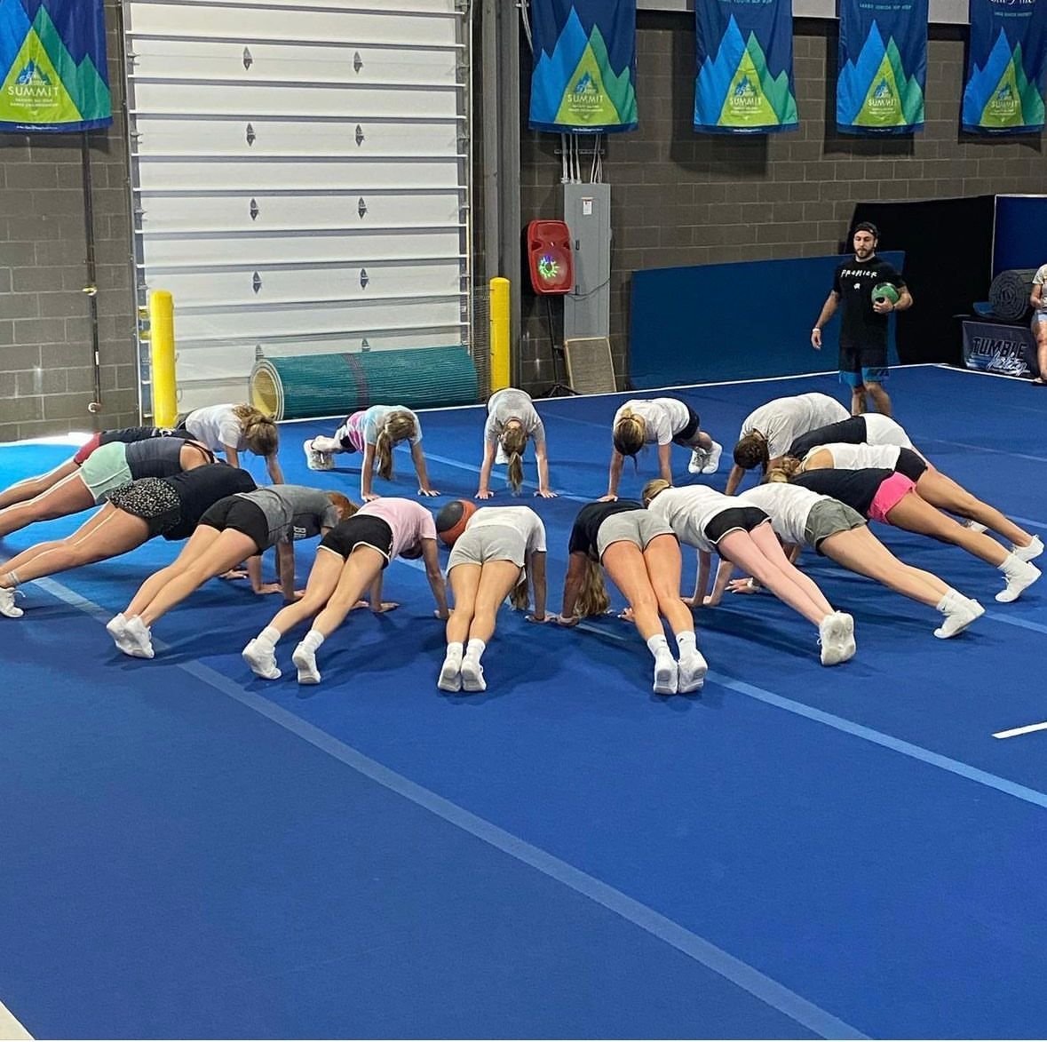 A group of cheerleaders are doing push ups on a blue mat.