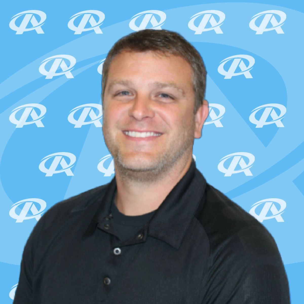 A man in a black shirt is smiling in front of a blue background with the letter r on it
