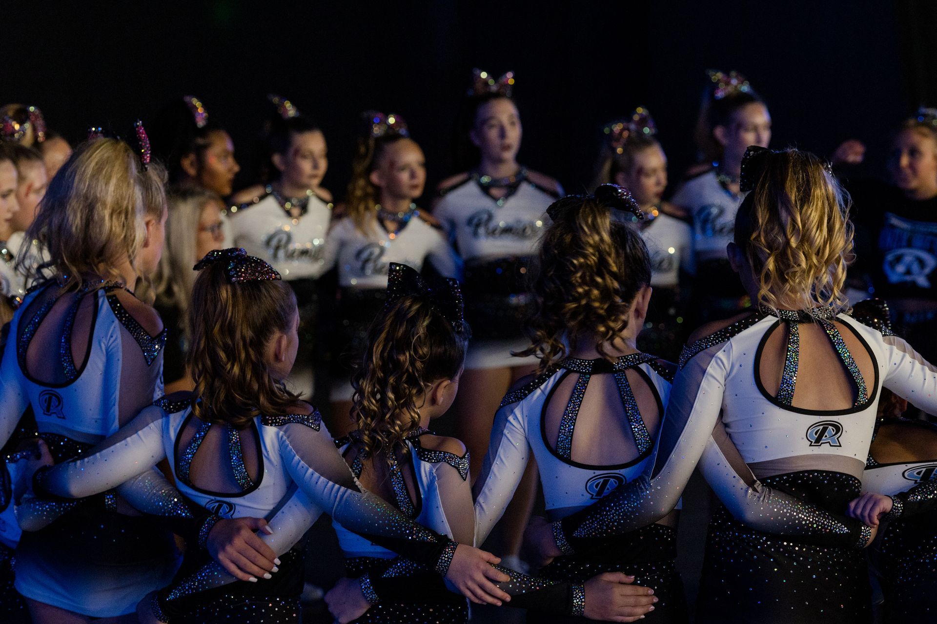 A group of cheerleaders are sitting in a circle in a dark room.