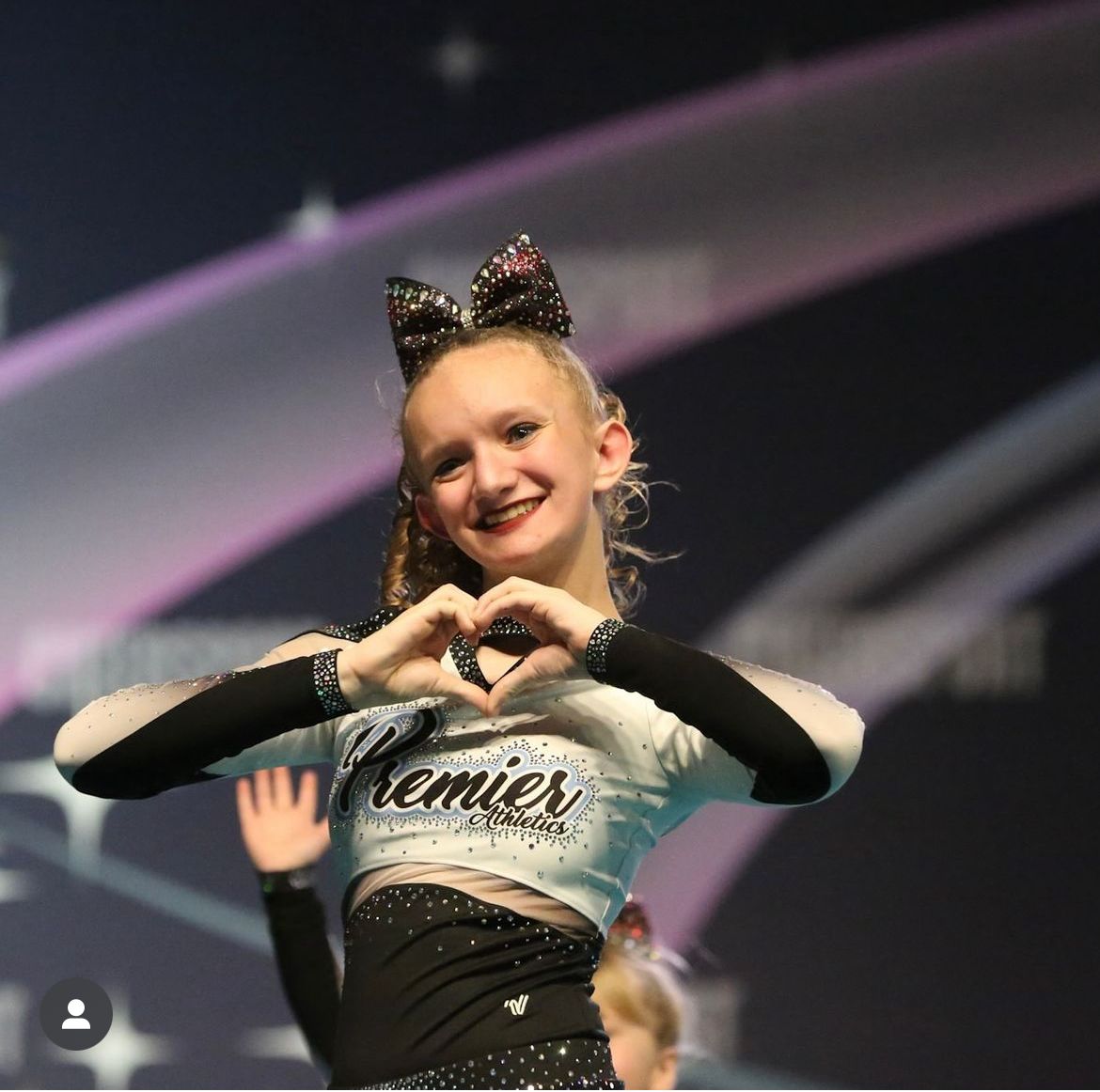 A cheerleader wearing a premier shirt makes a heart shape with her hands