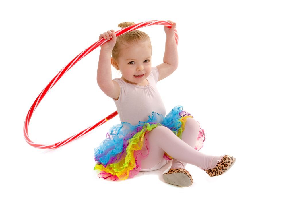 A little girl is sitting on the floor holding a red hula hoop.