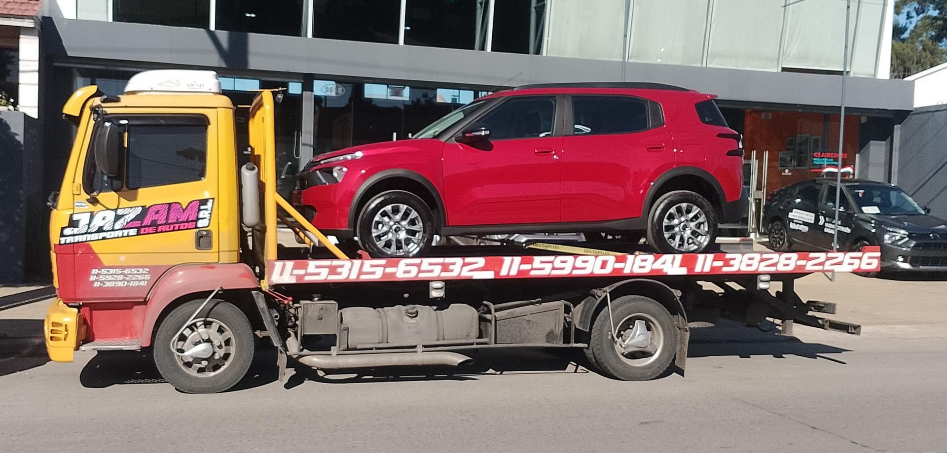 Un camión transportador de automóviles transporta varios SUV nuevos en una autopista, bajo la brillante luz del sol.