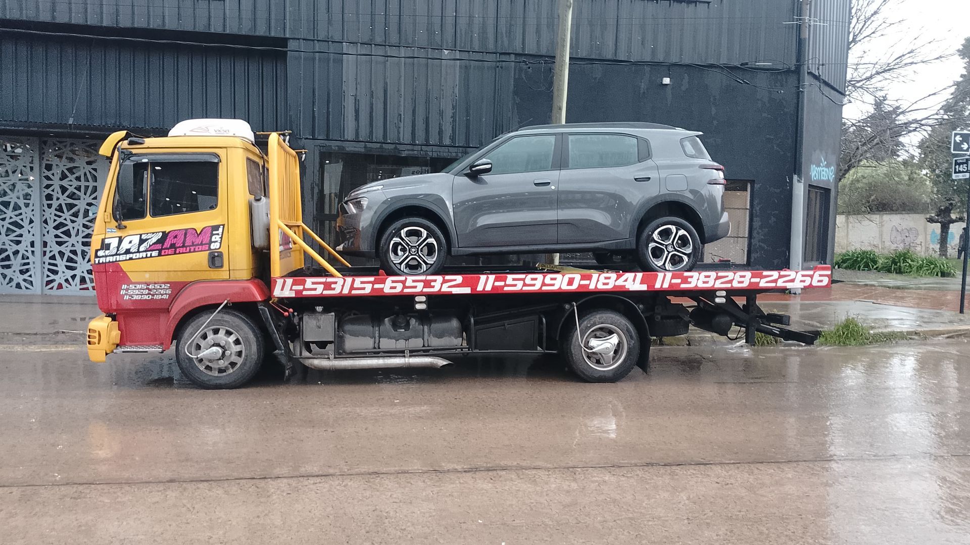 Un camión transportador de automóviles transporta varios vehículos blancos en una carretera pavimentada bajo un cielo azul.
