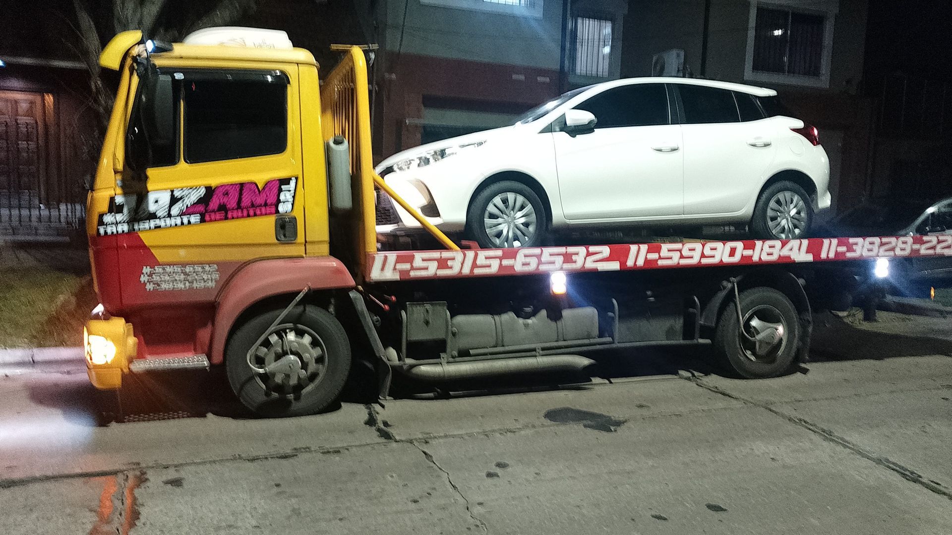 Un camión blanco que transporta coches blancos nuevos en un día soleado en un entorno al aire libre.