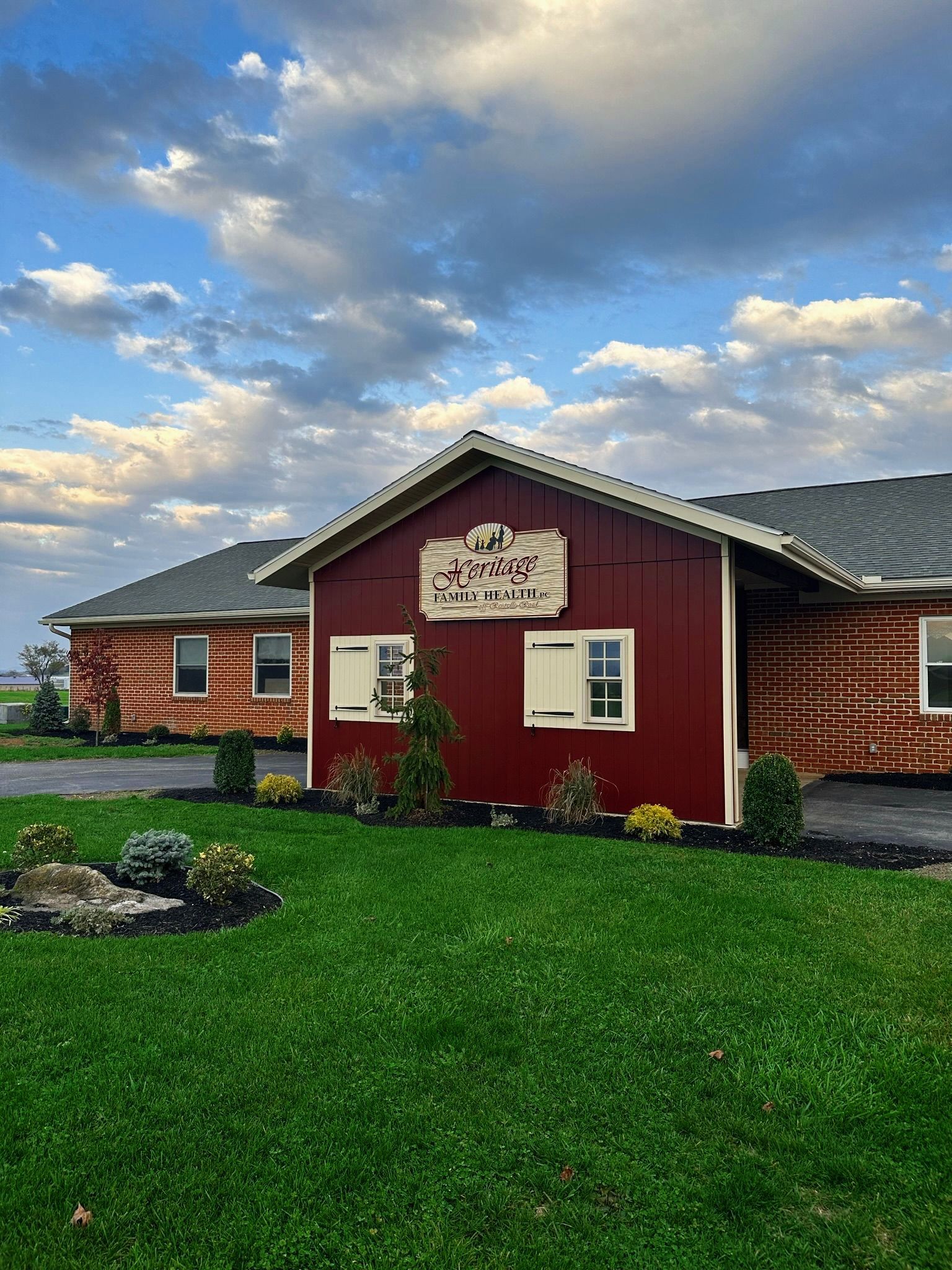 Red and brown building with white trim, sign above windows, on green lawn, cloudy sky.