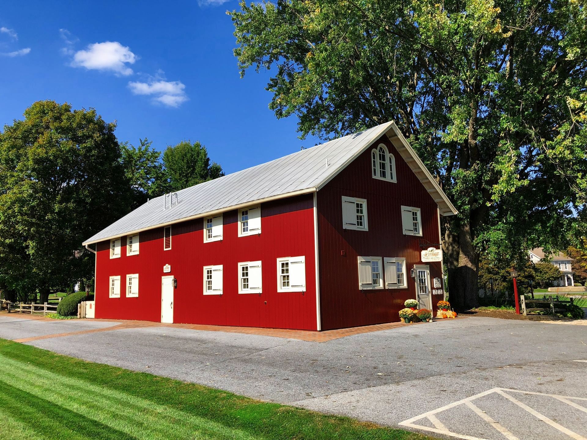 Red barn with white trim, gray roof, and surrounding greenery on a sunny day.