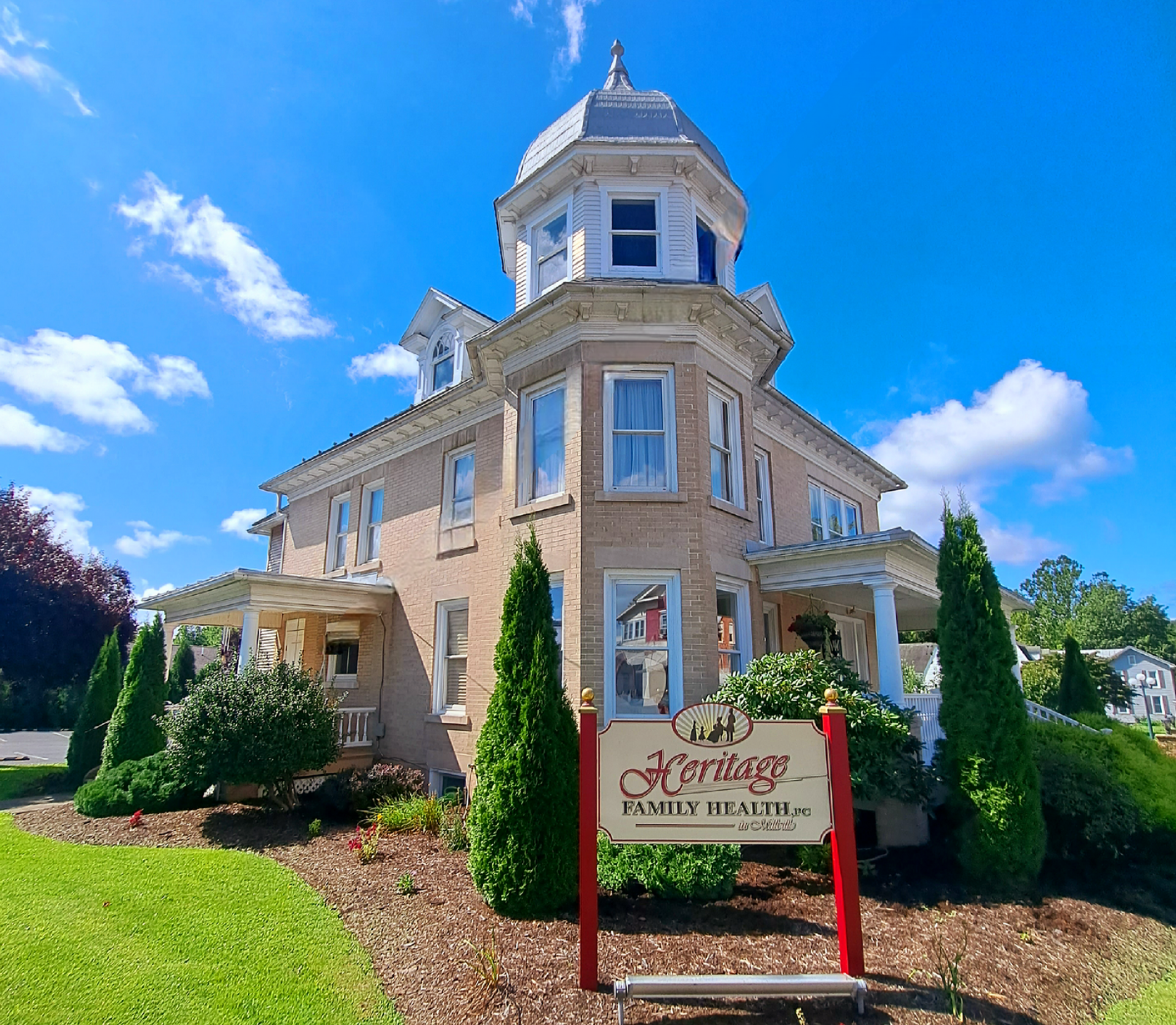Heritage Family Health building with sign, light brick, turret, and green lawn under a blue sky.