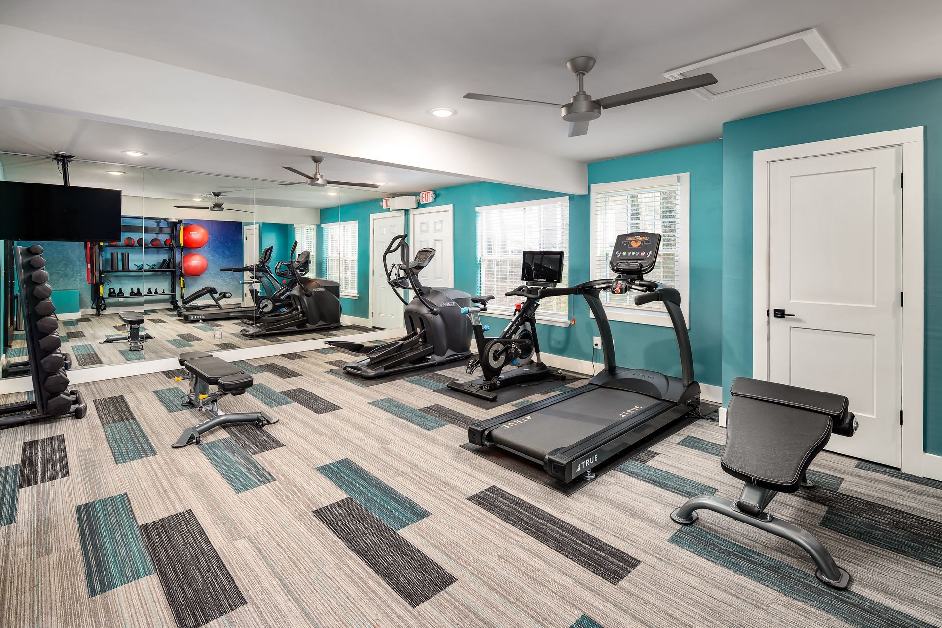 A gym with treadmills , exercise bikes , and a ceiling fan.