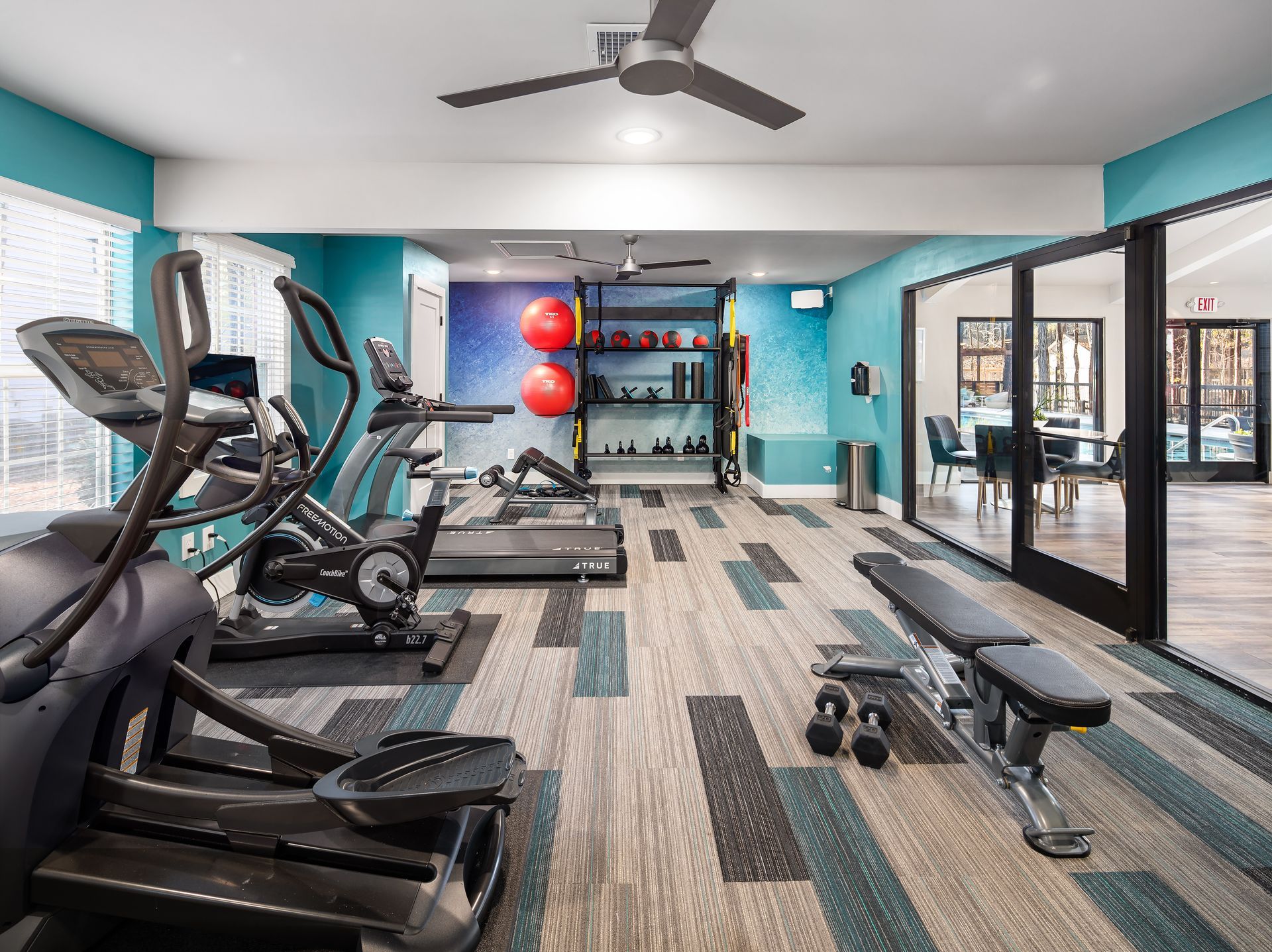A gym with a lot of equipment and a ceiling fan.