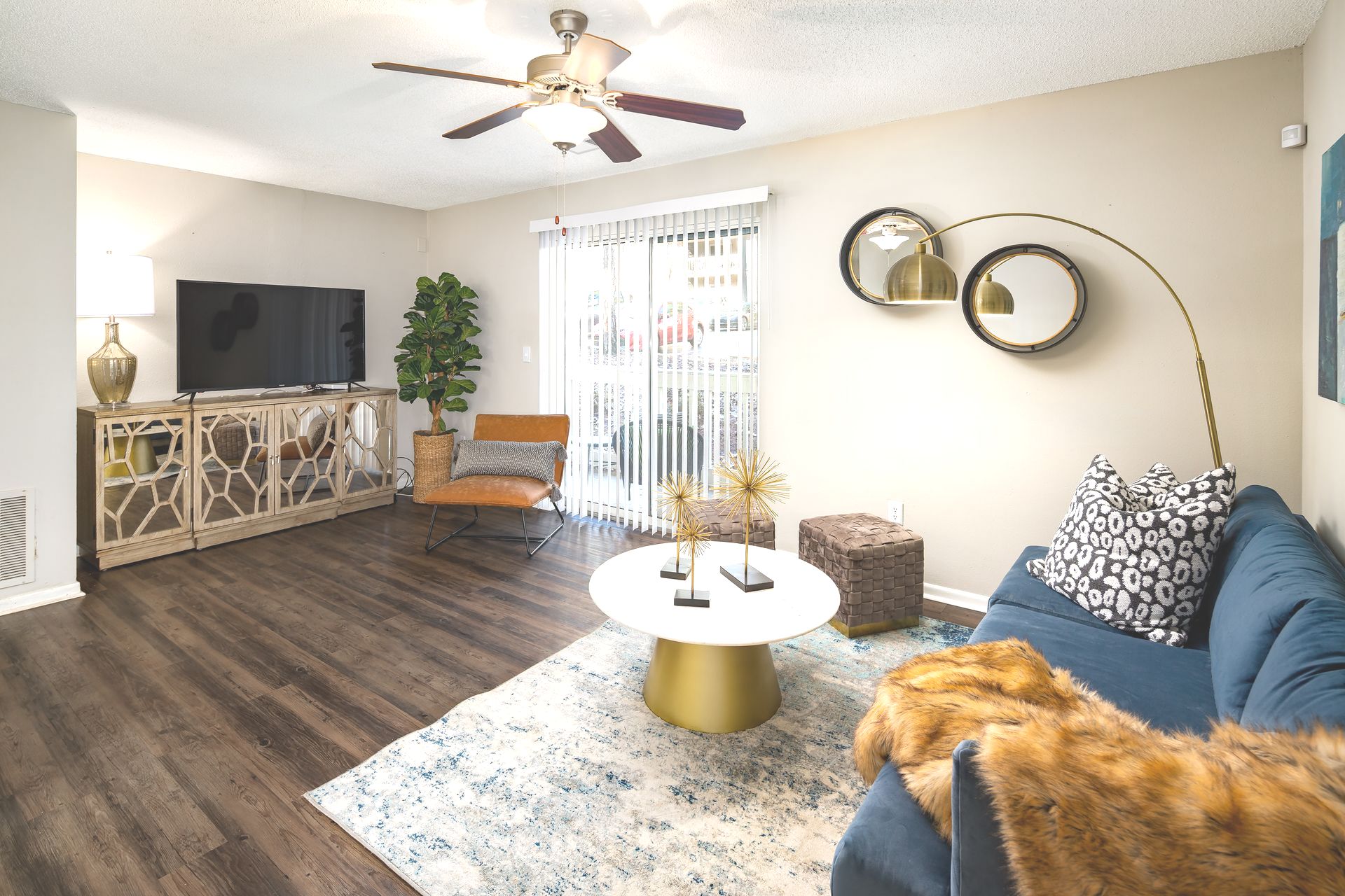 A living room with a couch , chair , coffee table , television and ceiling fan.