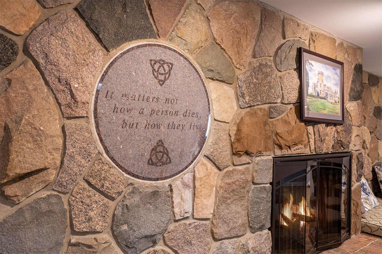 Stone wall with fireplace and inscription on round plaque.