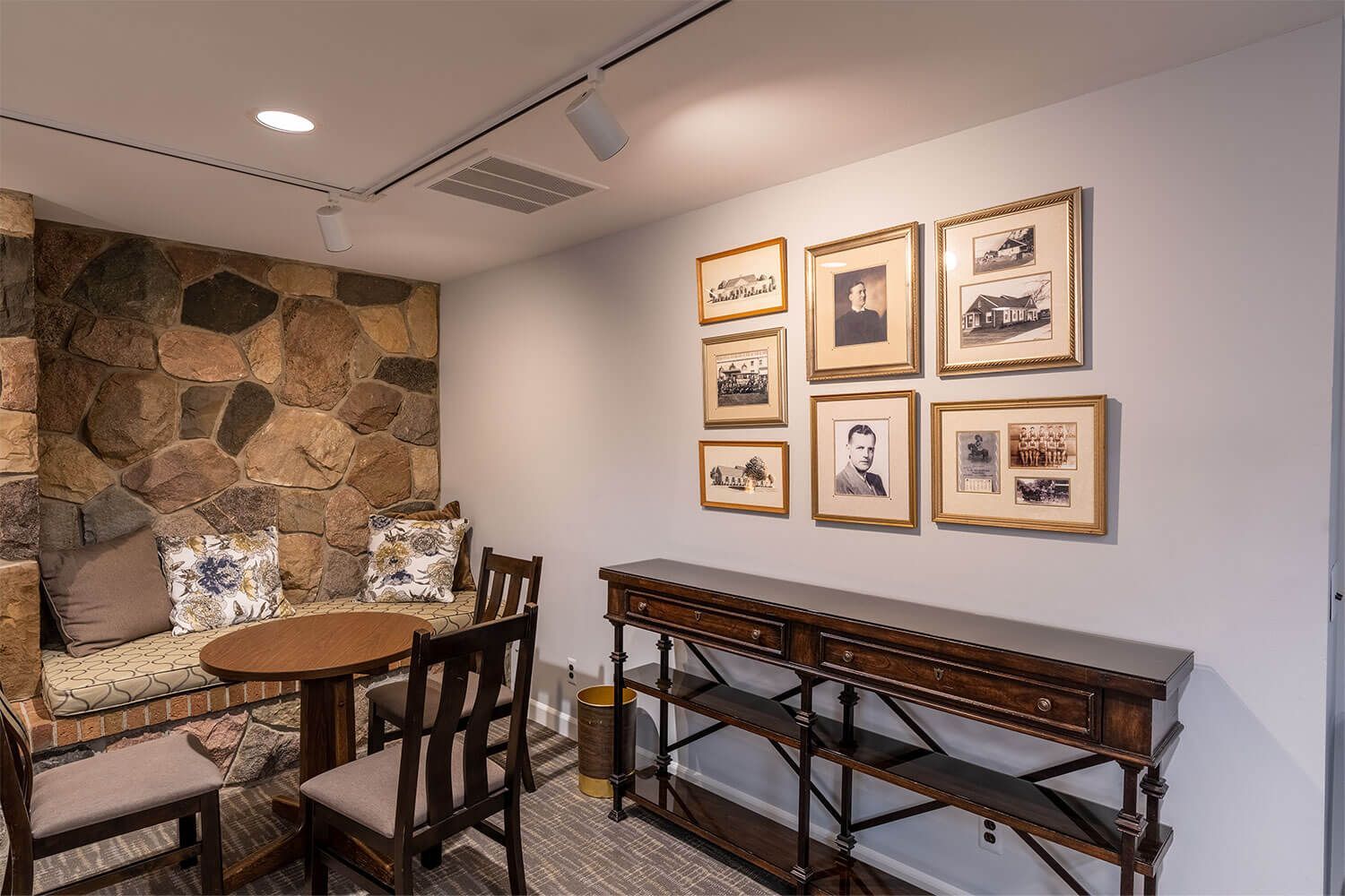 Cozy sitting area with stone wall, round table, chairs, and framed vintage photos.