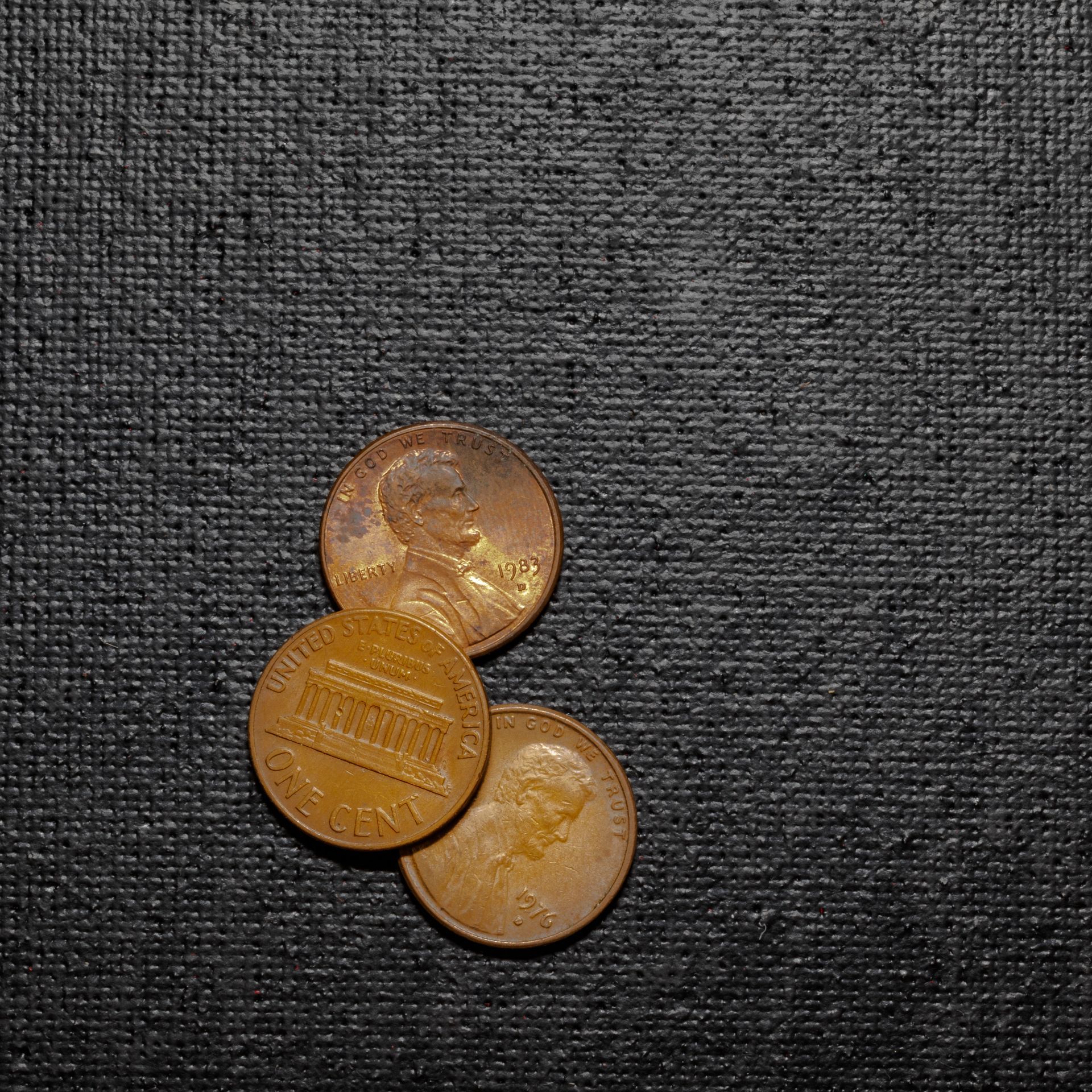 Three US pennies on a textured black surface.