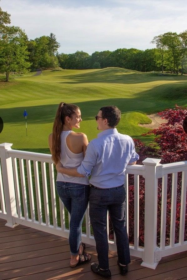 A man and a woman are standing on a balcony overlooking a golf course.
