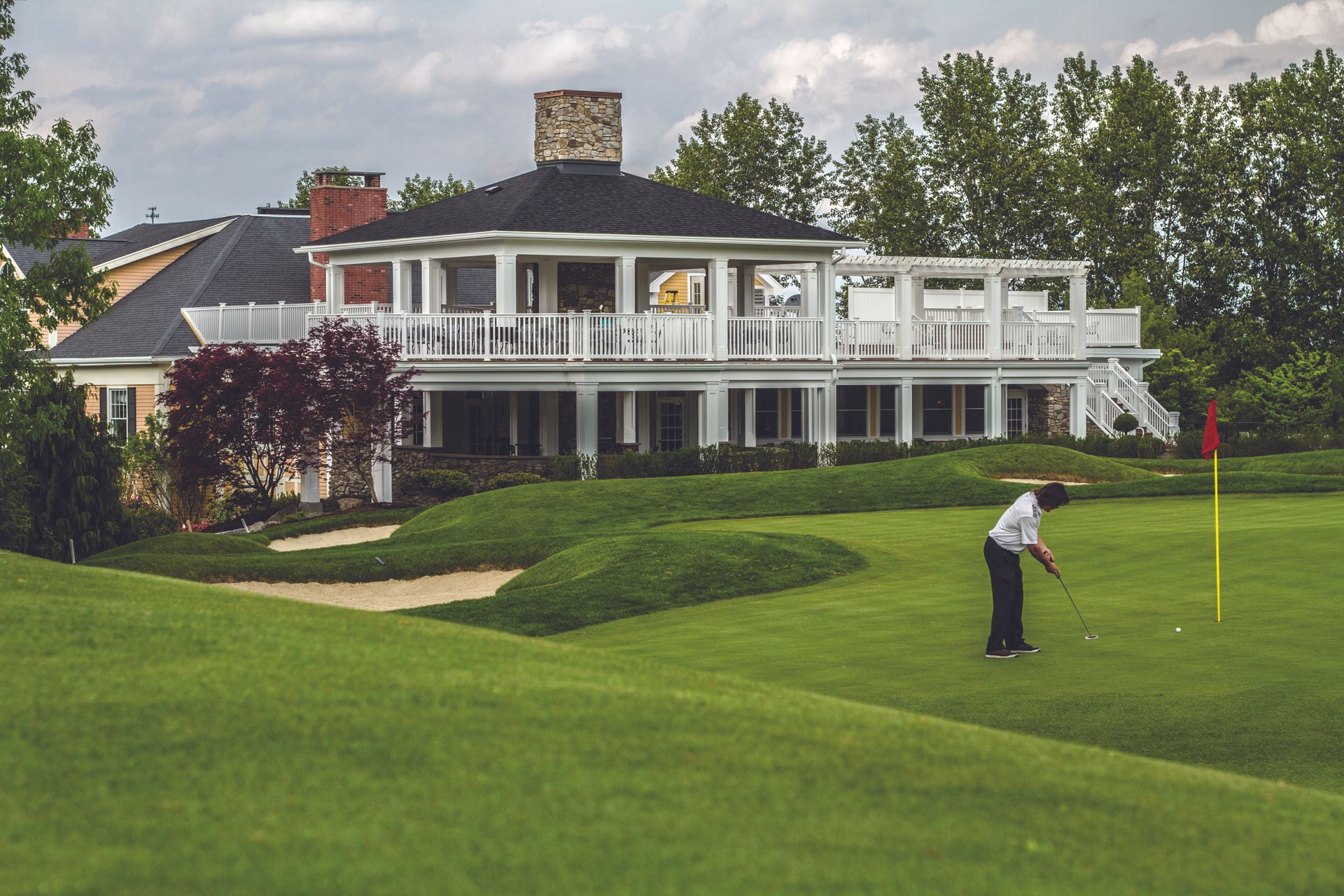 A man is putting on a golf course in front of a large house