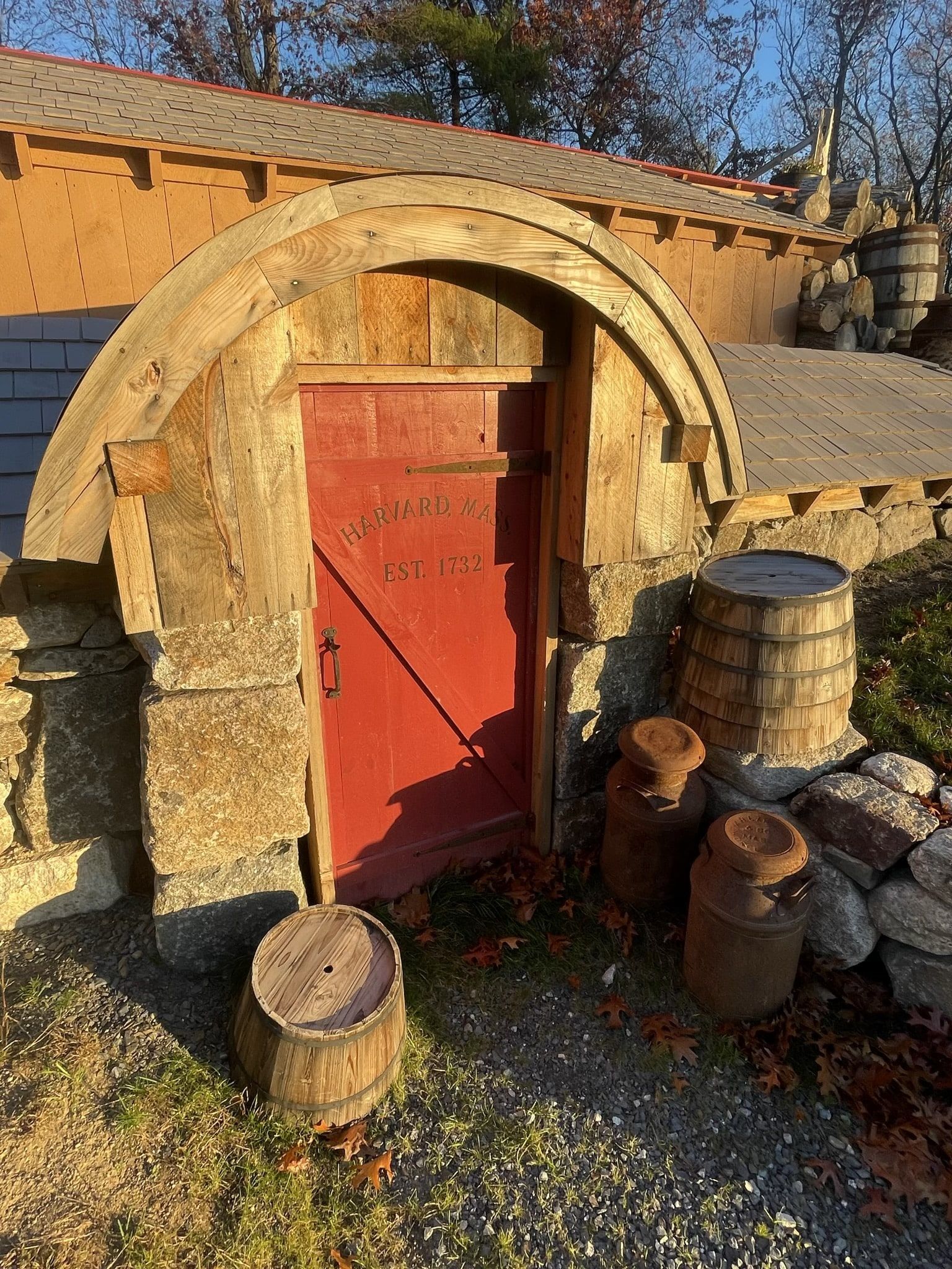 A red door is surrounded by wooden barrels and a stone archway.