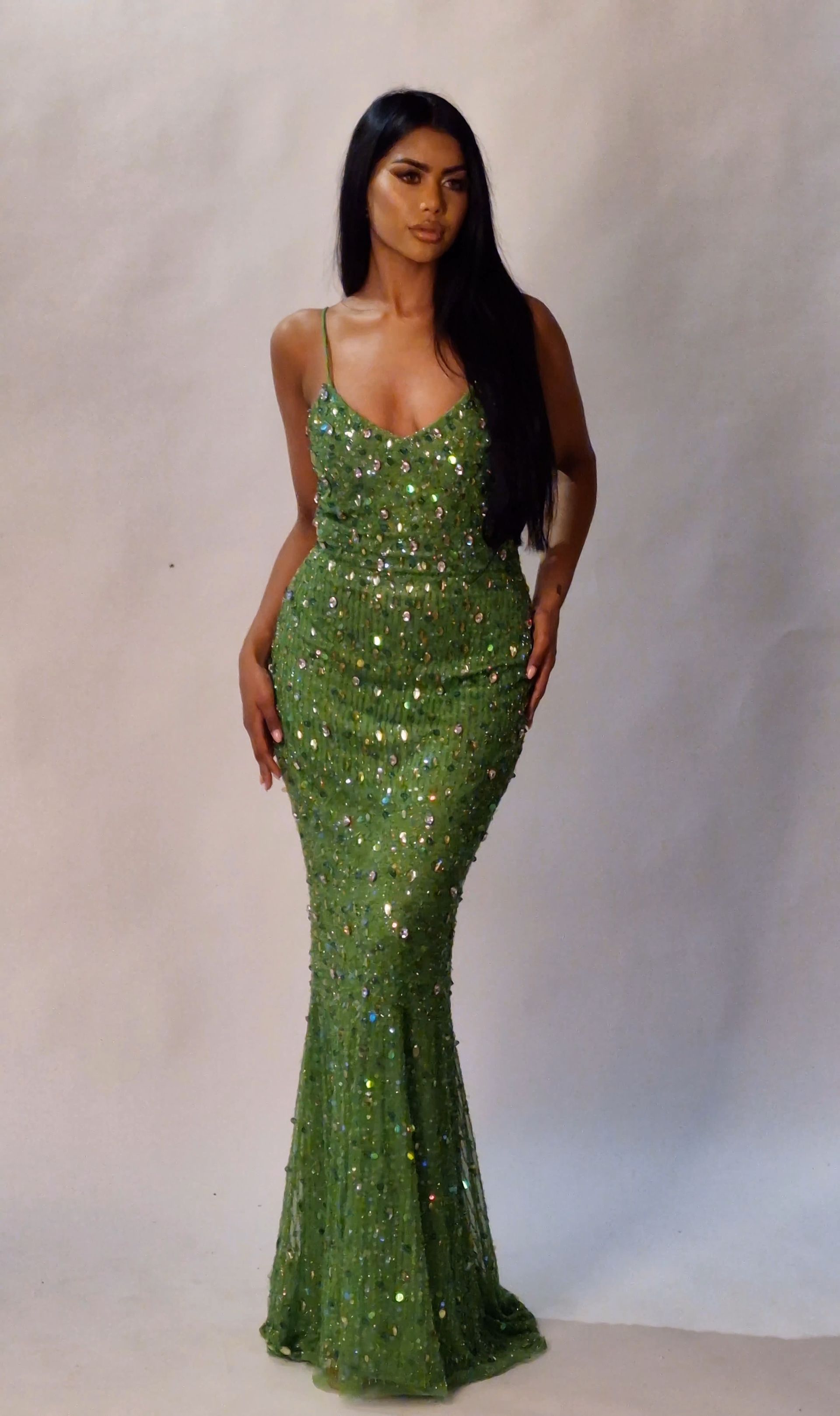 Vrouw in een glinsterende groene jurk, staand voor een lichte achtergrond.