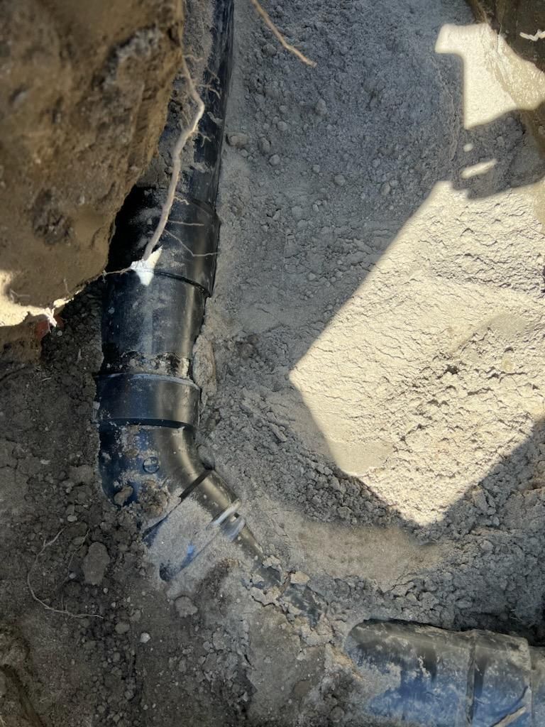 A Black Pipe is Laying in the Dirt in a Hole