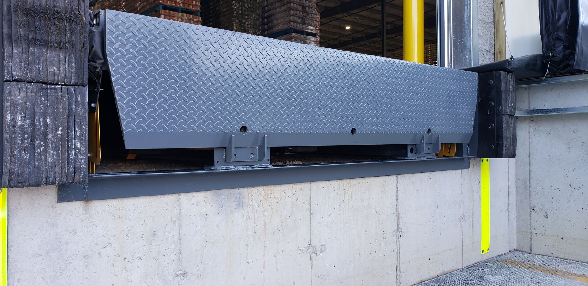 A loading dock with a metal ramp extending out. The ramp has a diamond plate surface and is attached to a concrete wall.