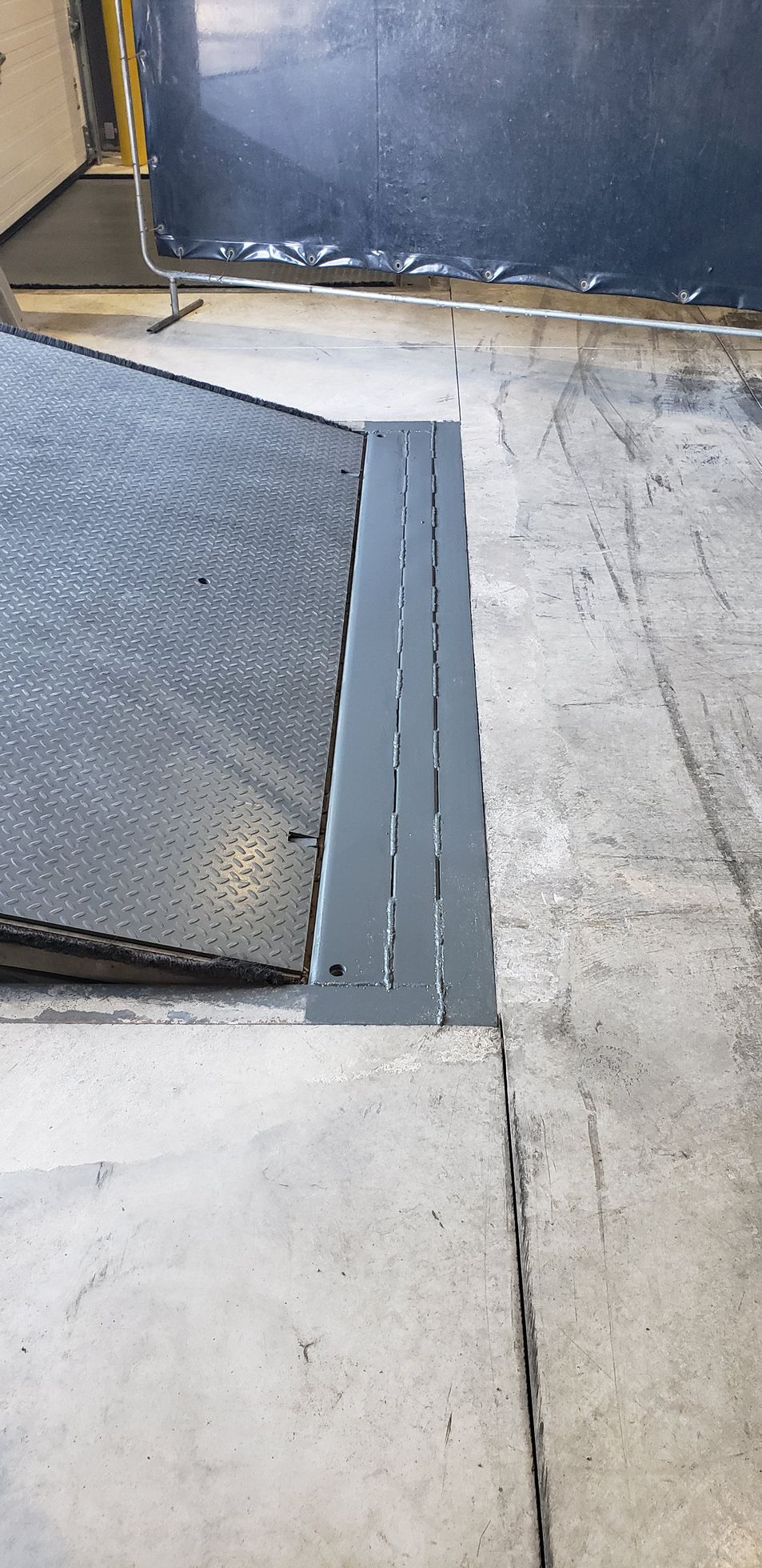A gray metal ramp with slots is next to a concrete floor. The ramp is at a loading dock.