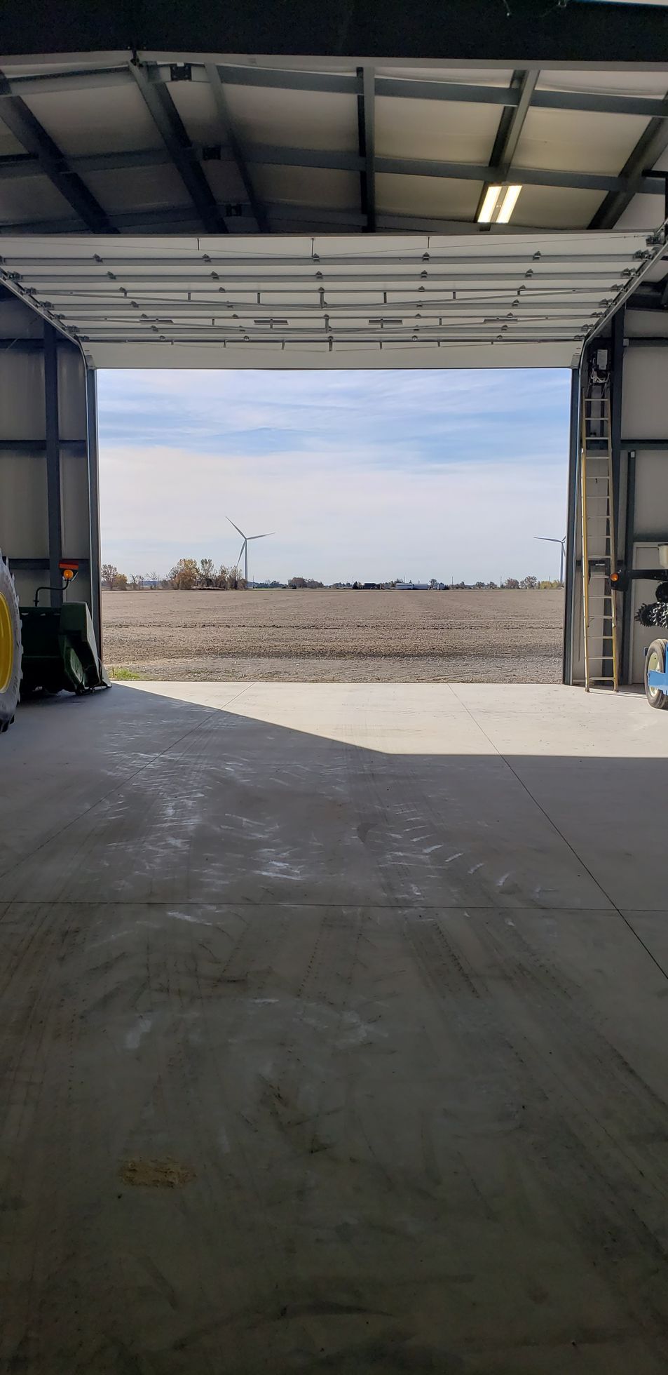 Open doorway reveals a vast, overcast field under a cloudy sky. Inside is a concrete floor and metal frame.
