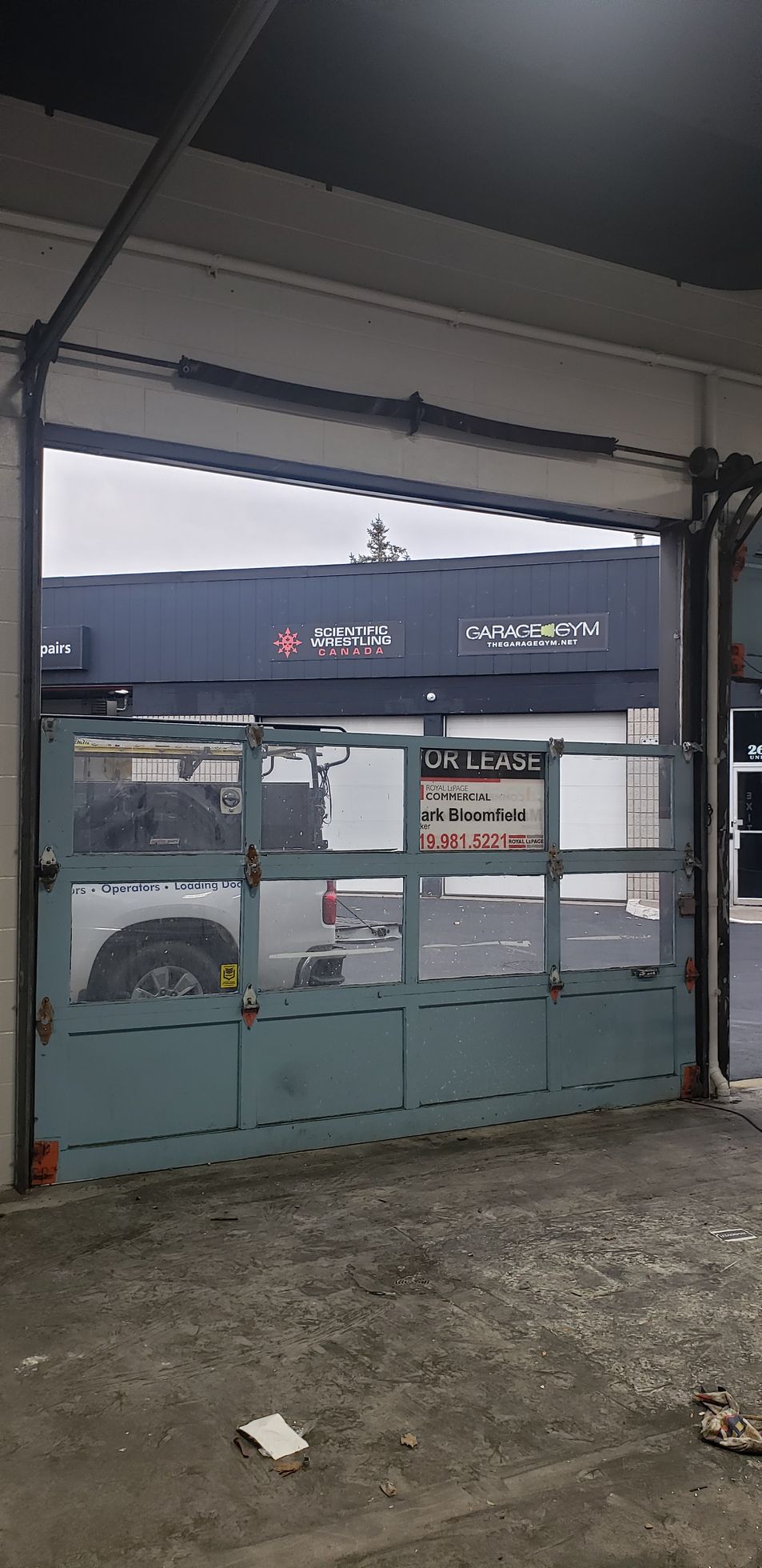 A partially open, metal-framed garage door with glass panels reveals a service shop and a white pickup truck inside.