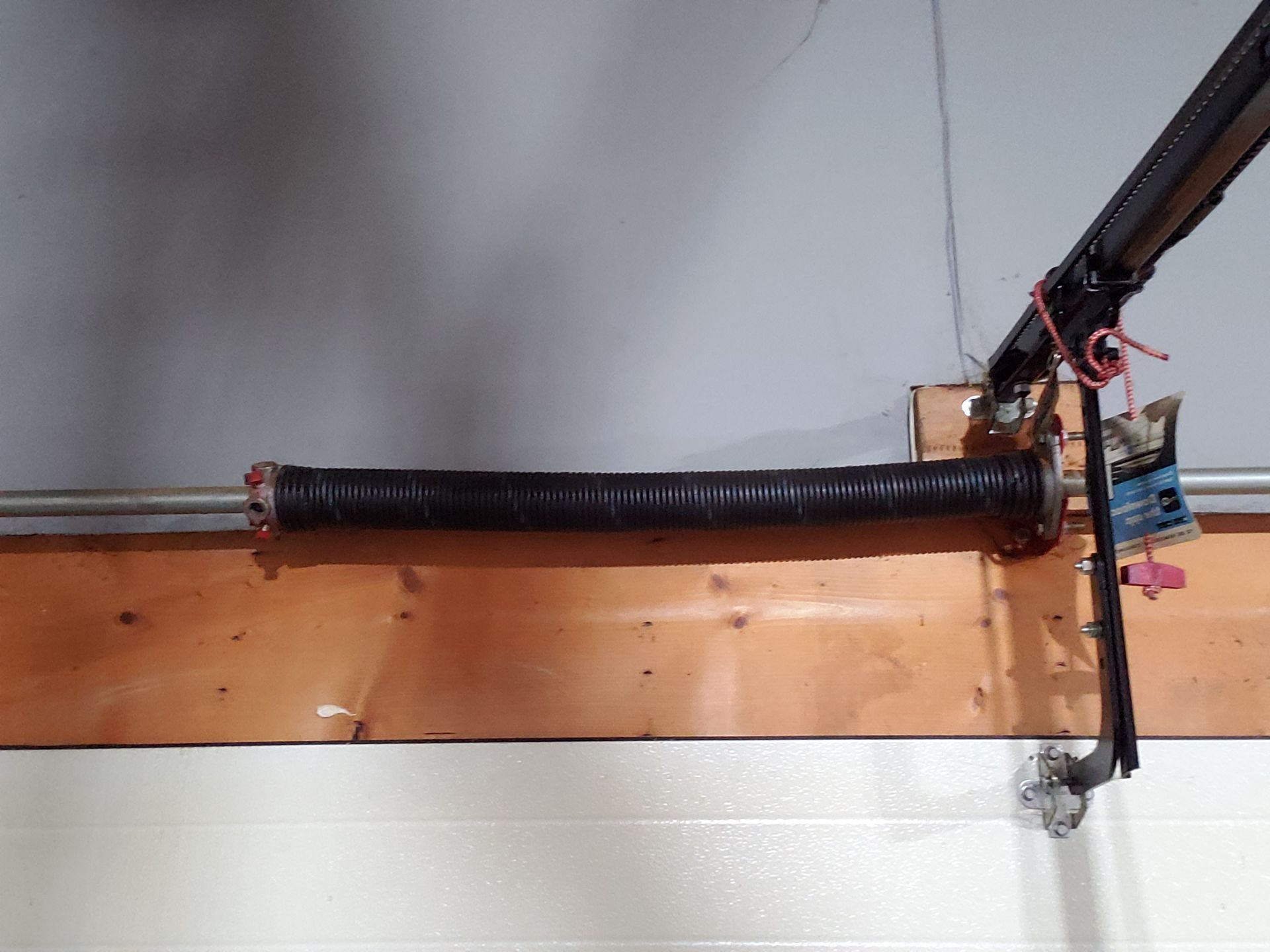 Garage door torsion spring, black, mounted above the garage door, on a wooden header.