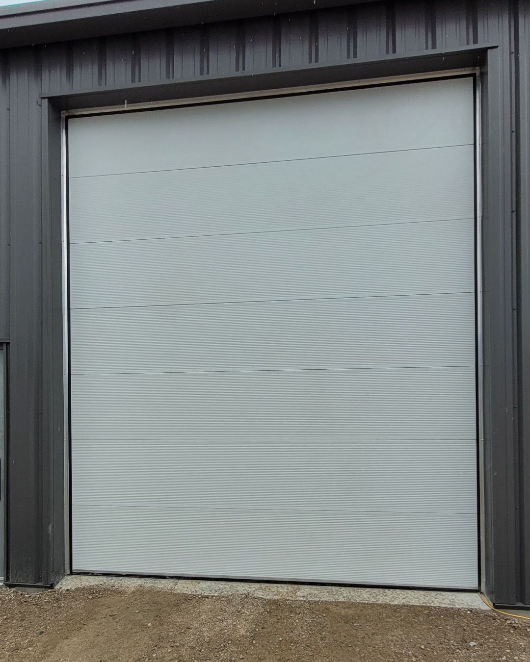 A closed, light gray overhead garage door set in a dark gray metal building.