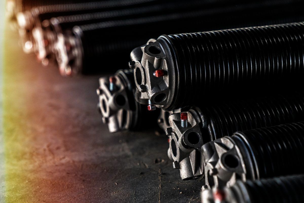 Black garage door torsion springs in a row, against a dark backdrop. The ends have metal hardware.