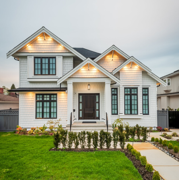 A two-story white house with dark window frames, a peaked roof, and a front porch with a dark wooden door.