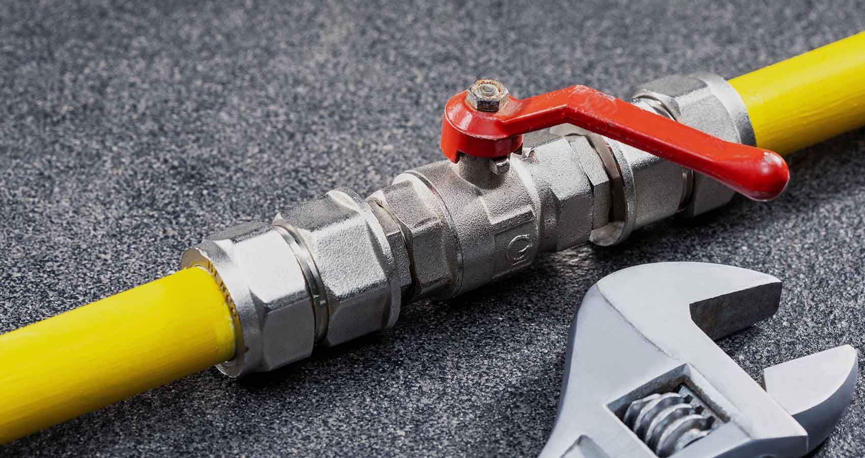 A close up of a gas pipe with a wrench next to it.