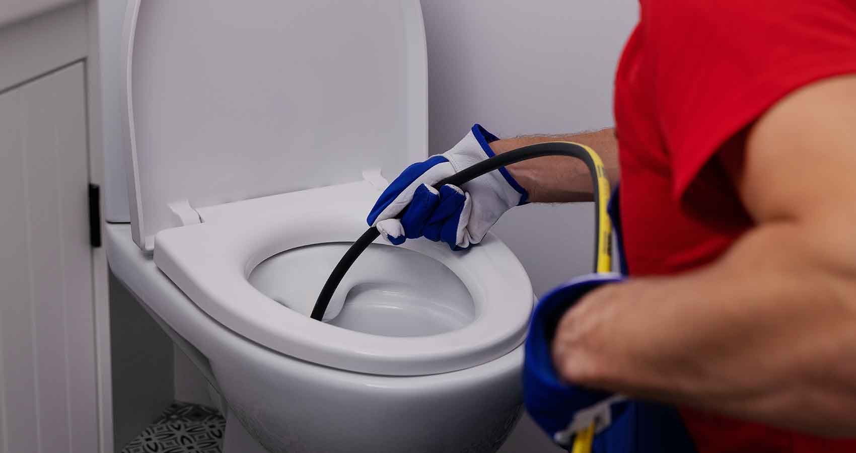 A man is cleaning a toilet with a hose.