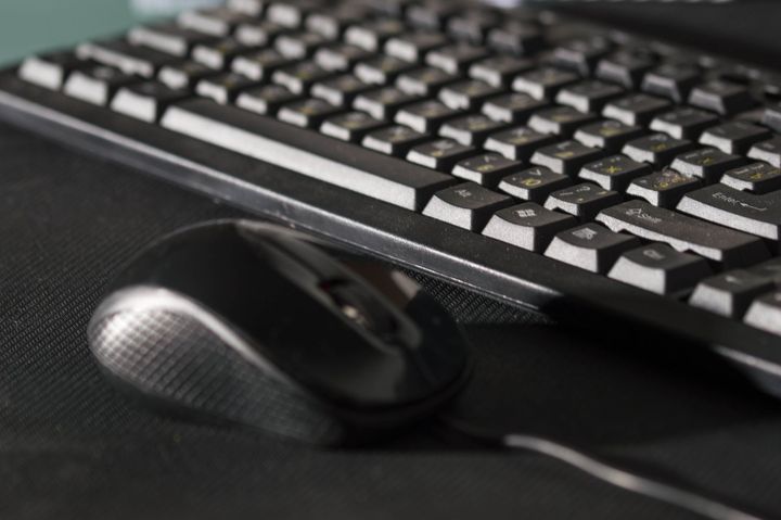 Un mouse nero per computer è appoggiato su un tappetino scuro e ruvido, accanto a una tastiera nera.