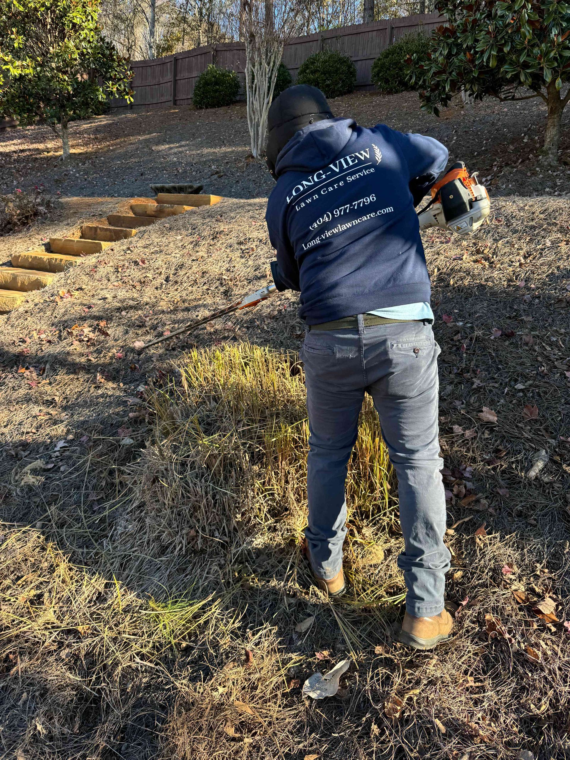 A man is mowing the lawn in front of a large brick house.