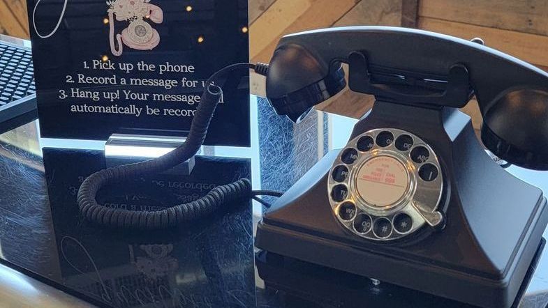 A black telephone is sitting on a table next to a sign