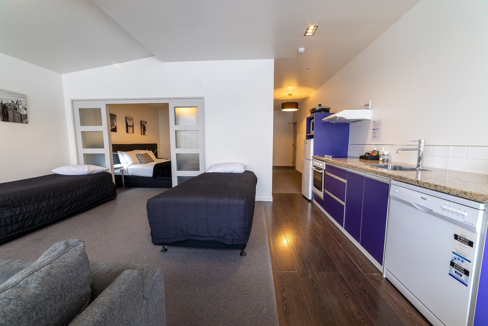 A bedroom with two beds and a kitchen with purple cabinets