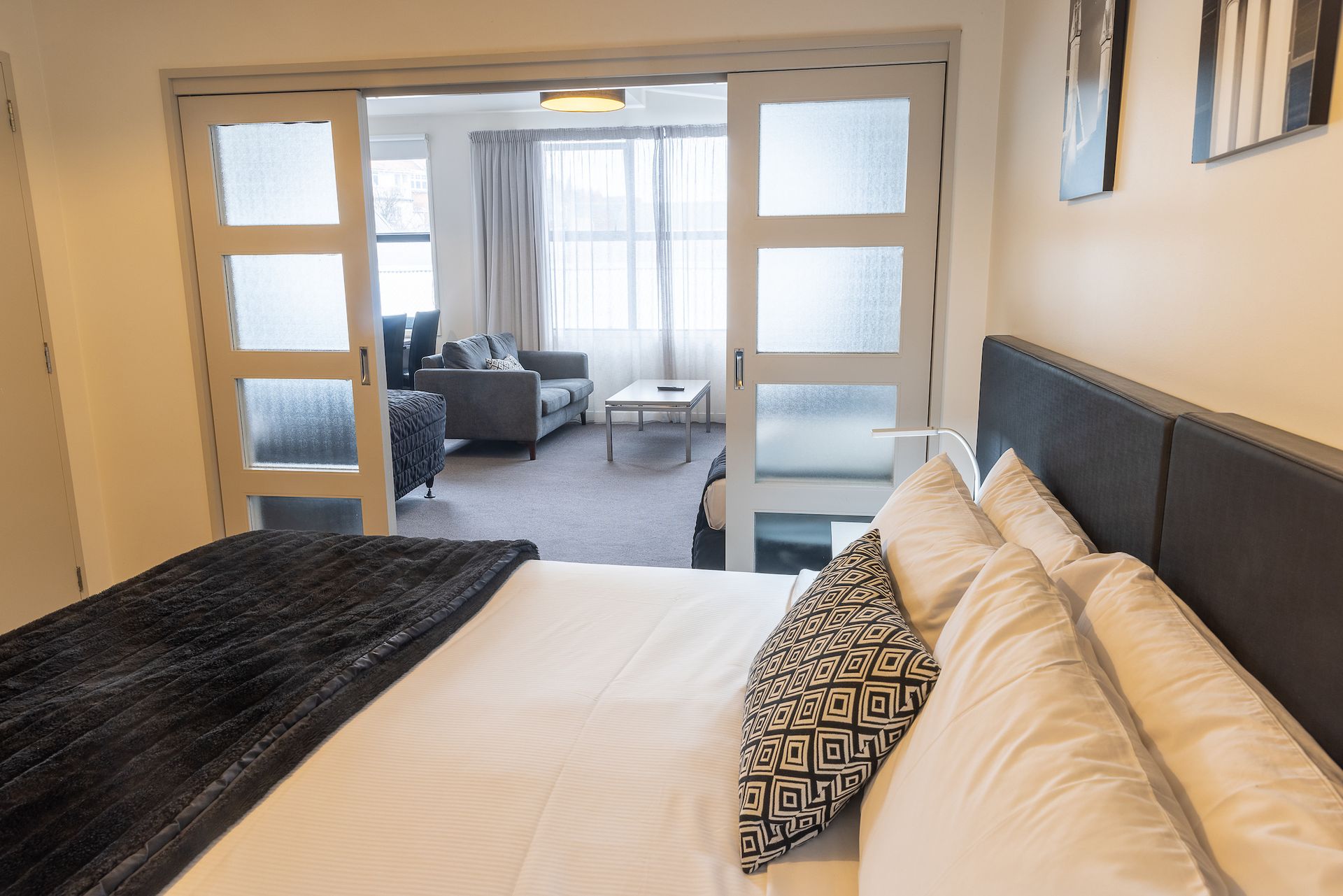 A bedroom with a king size bed and sliding glass doors leading to a living room.