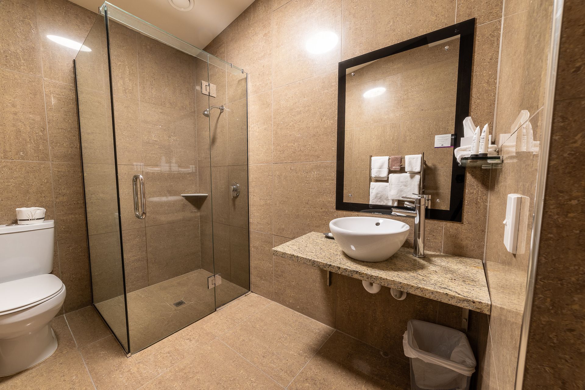 A bathroom with a toilet , sink , mirror and walk in shower.