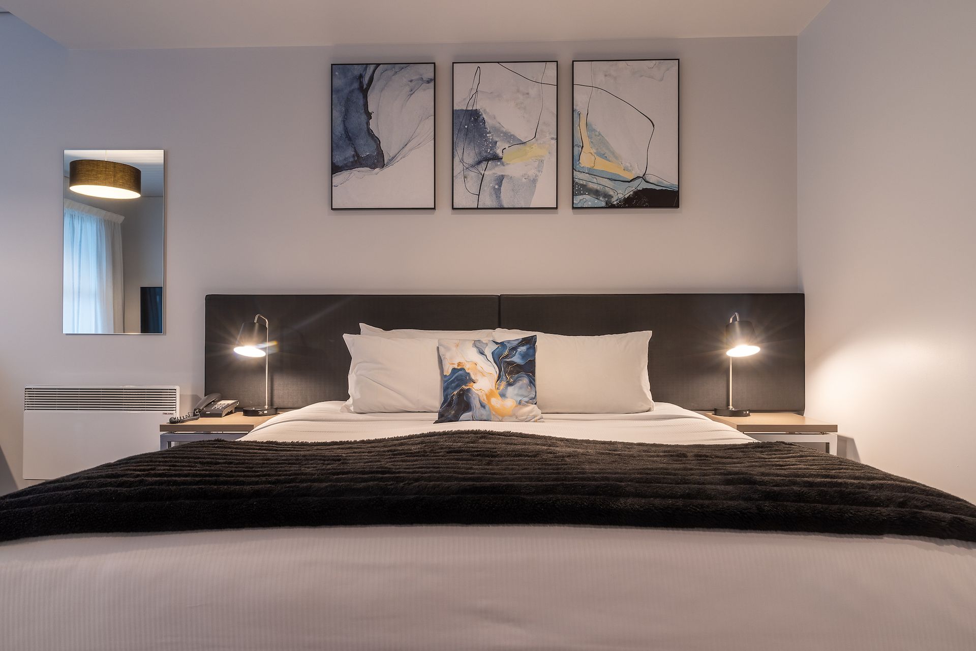 A bedroom with a large bed and three paintings on the wall.