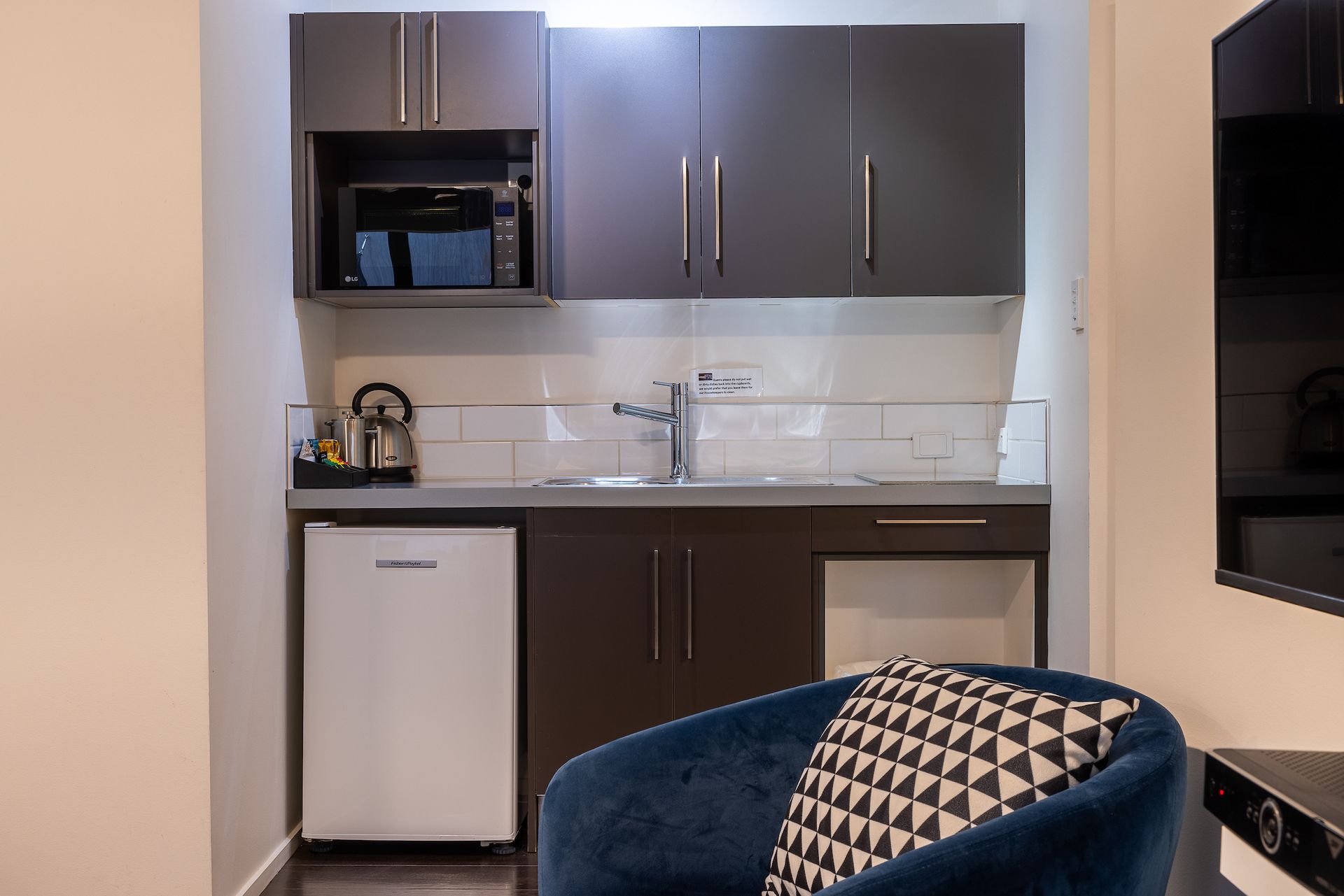 A small kitchen in a hotel room with a chair and a television.