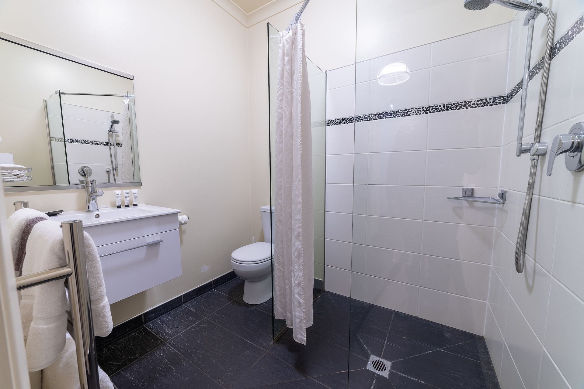 A bathroom with a toilet , sink , shower and mirror.