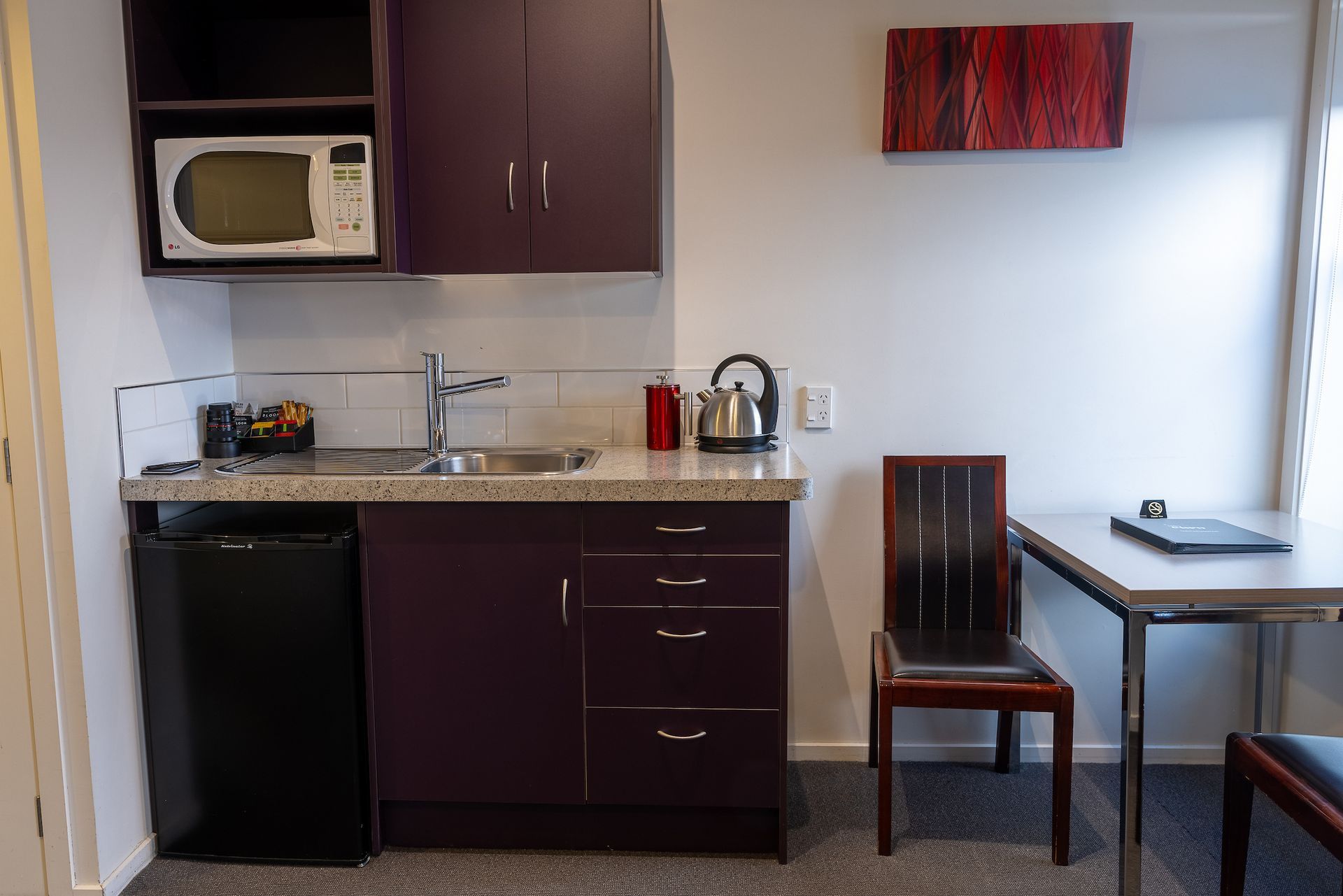 A small kitchen with purple cabinets and a microwave