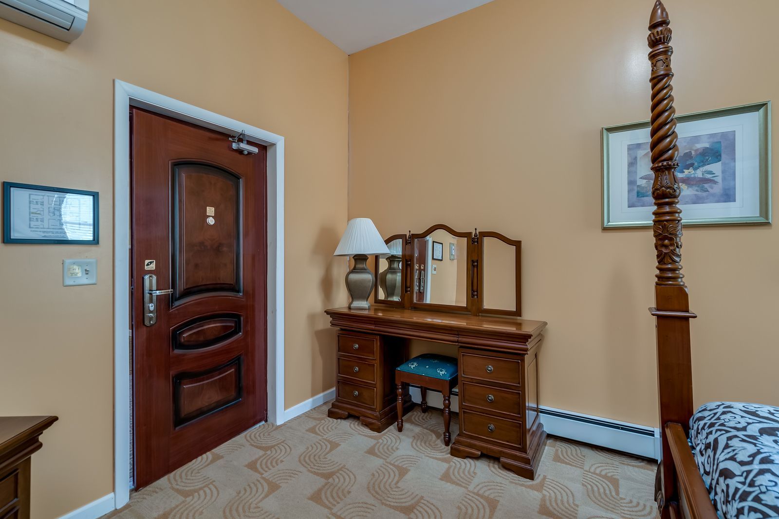 A bedroom with a four poster bed , dresser , mirror and lamp.