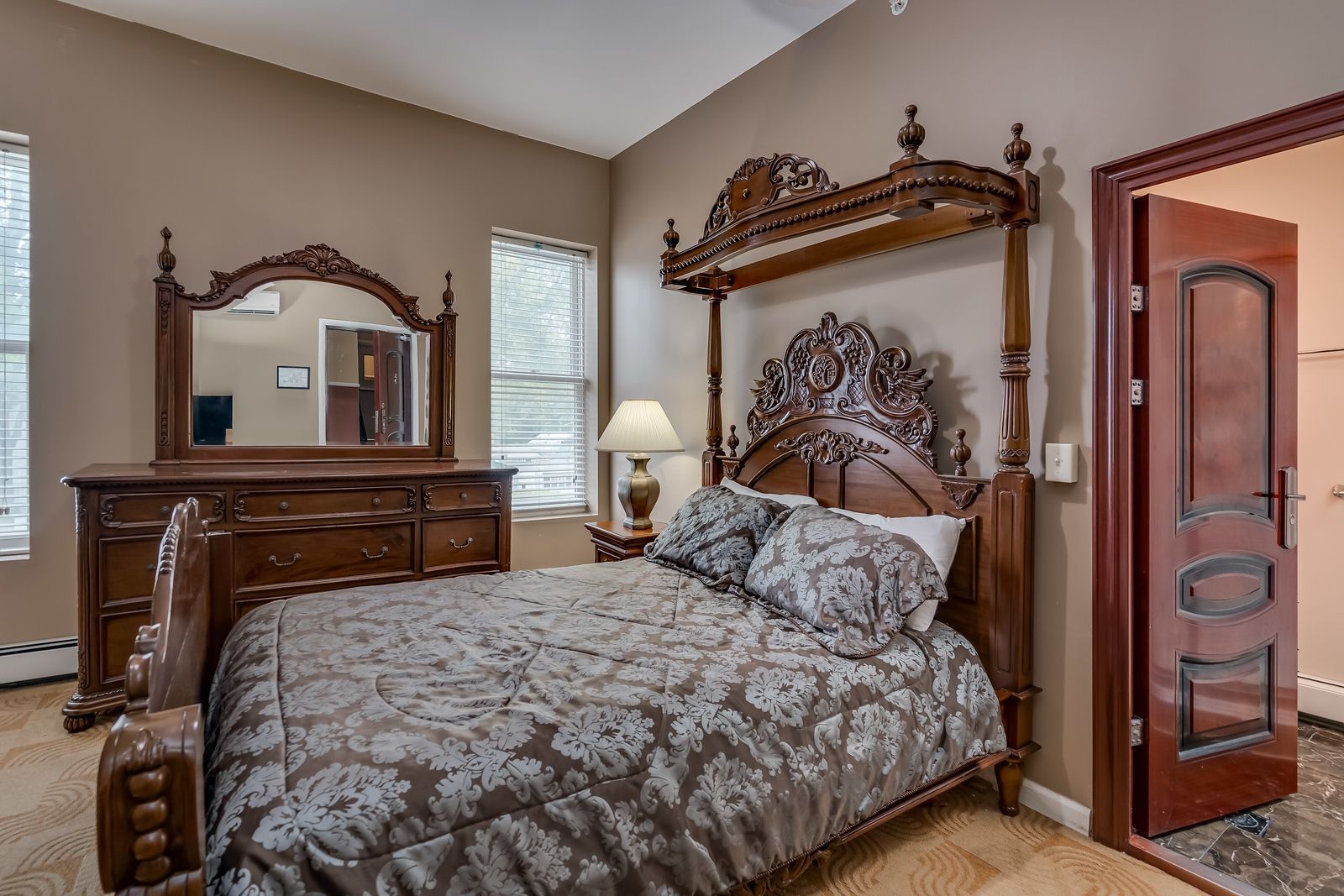 A bedroom with a four poster bed , dresser , mirror and lamp.