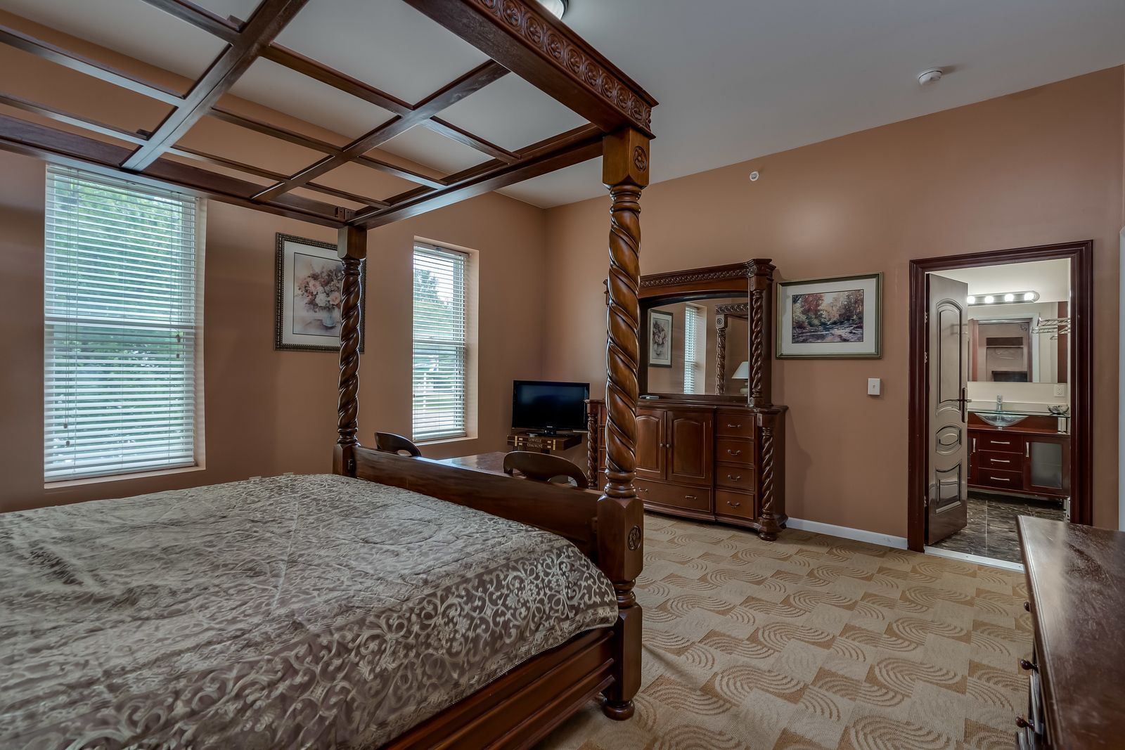 A bedroom with a four poster bed , dresser , mirror and television.